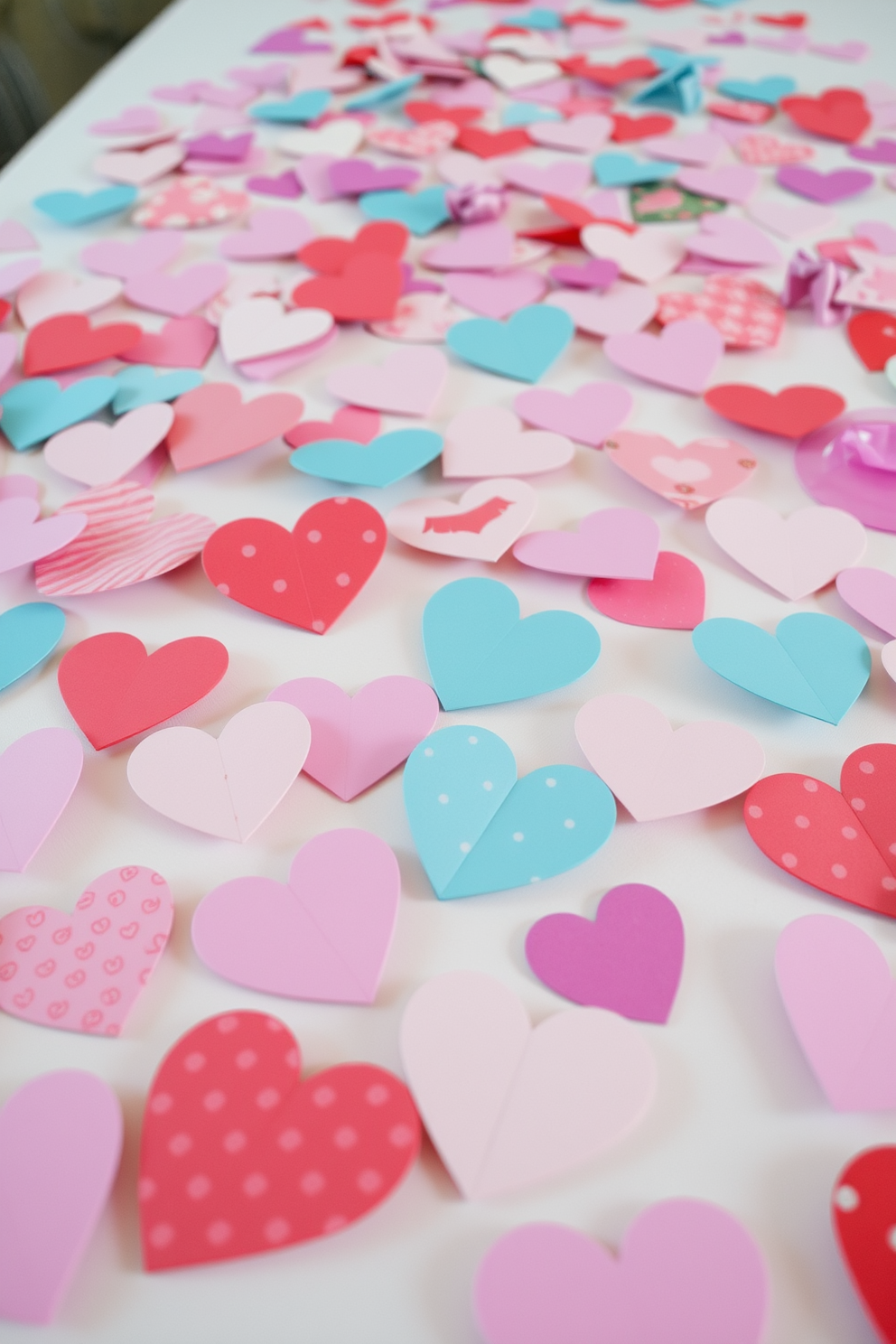 Colorful paper hearts scattered across tables create a festive and romantic atmosphere. Each heart features unique patterns and colors, adding a playful touch to the Valentine's Day decor.