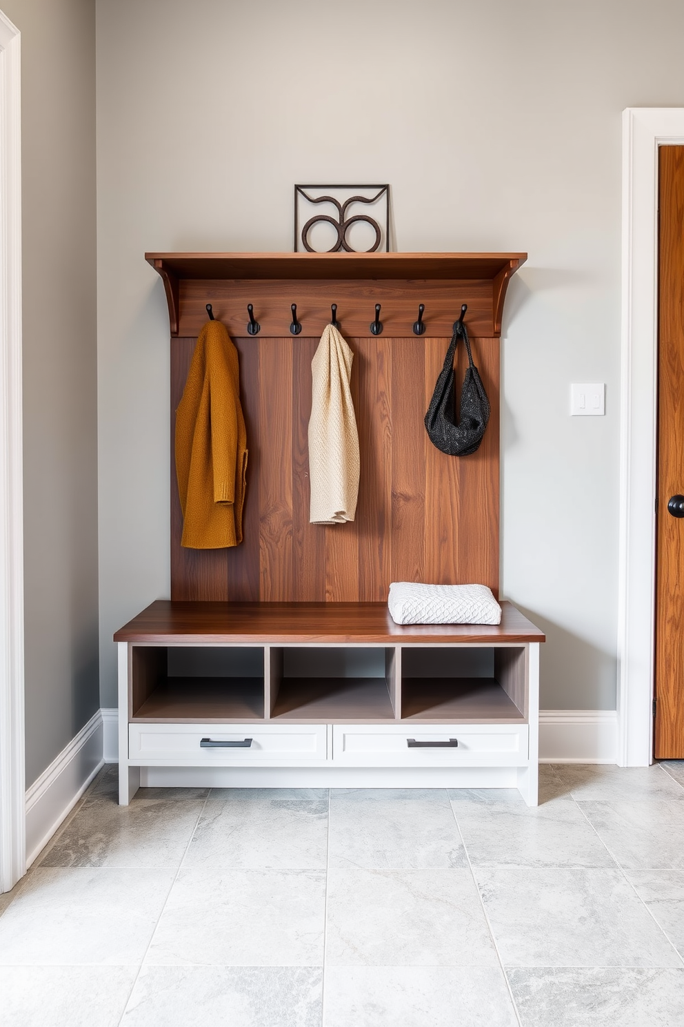 A sleek bench with hidden storage compartments is positioned against a wall, providing a functional yet stylish seating area. The bench features a smooth finish in a rich walnut wood, seamlessly blending with the mudroom's elegant design. The mudroom is adorned with soft gray walls and a durable tile floor that mimics natural stone. Above the bench, a series of hooks and a decorative shelf create an organized space for coats and accessories, enhancing both utility and aesthetics.