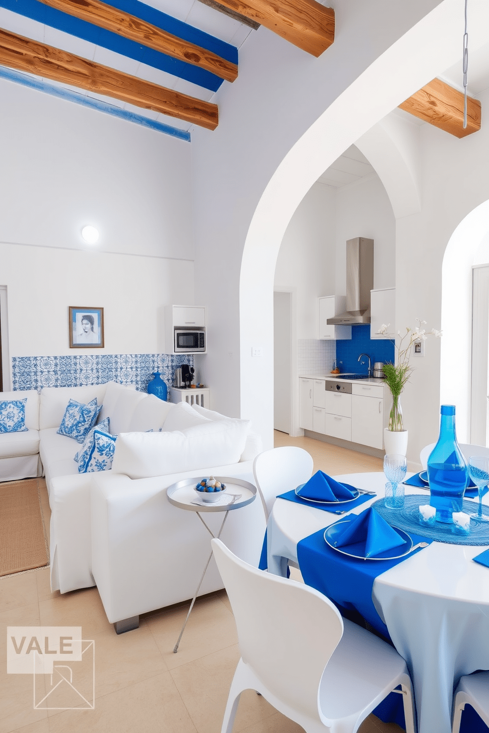 A bright and airy Mediterranean apartment featuring a vibrant blue and white color scheme. The living room showcases whitewashed walls adorned with blue ceramic tiles, complemented by comfortable white sofas with blue accent pillows. In the kitchen, sleek white cabinetry contrasts beautifully with a bold blue backsplash and rustic wooden beams overhead. The dining area includes a round table with white chairs, accented by a stunning blue and white table setting.