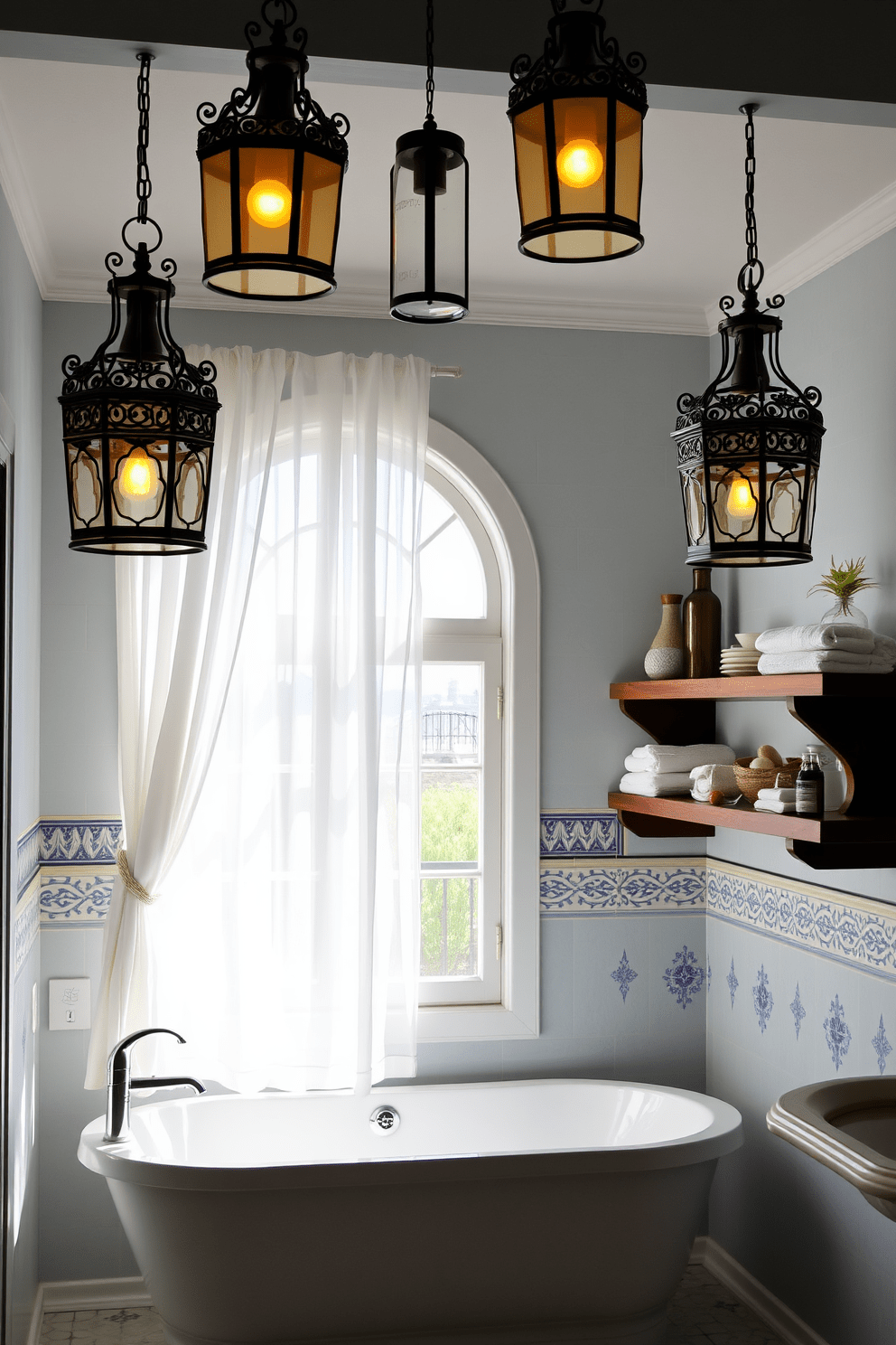 Mediterranean-inspired lanterns hang from the ceiling, casting a warm glow throughout the space. The walls are adorned with intricate tile work in shades of blue and white, enhancing the room's coastal charm. A spacious soaking tub is positioned under a large window, framed by sheer white curtains that flutter gently in the breeze. Rustic wooden shelves hold neatly rolled towels and decorative items, adding to the inviting atmosphere.