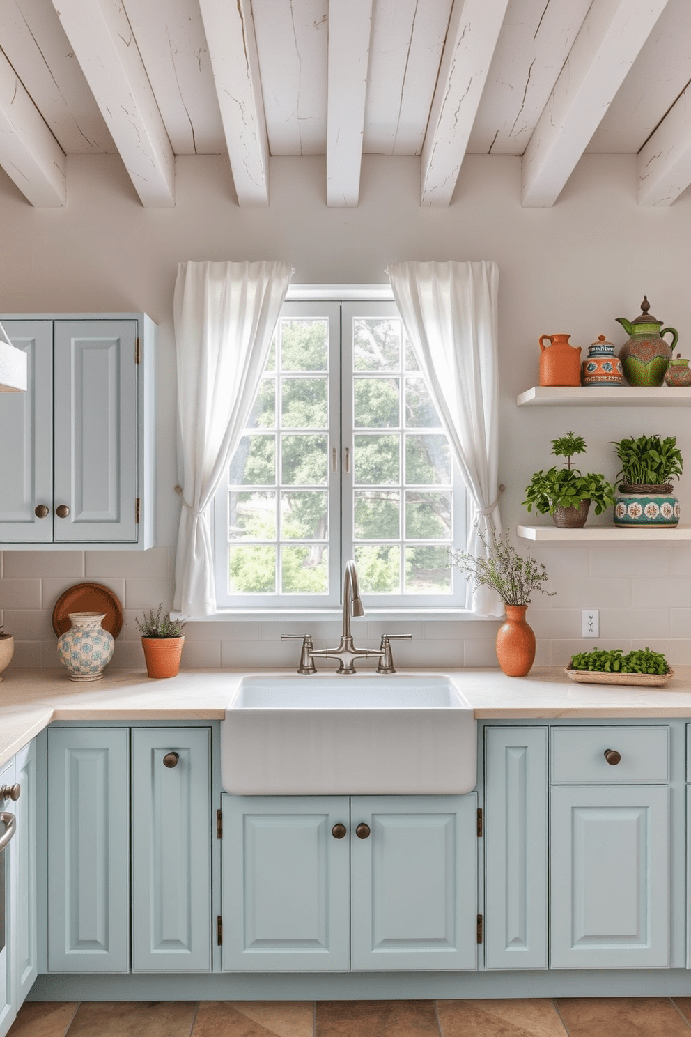 A Mediterranean kitchen with soft pastel colors creates a serene atmosphere. The cabinetry features light blue and soft pink hues, complemented by whitewashed wooden beams overhead. A large farmhouse sink sits beneath a window adorned with sheer curtains, allowing natural light to flood the space. The countertops are made of creamy marble, and rustic open shelving displays colorful pottery and fresh herbs.