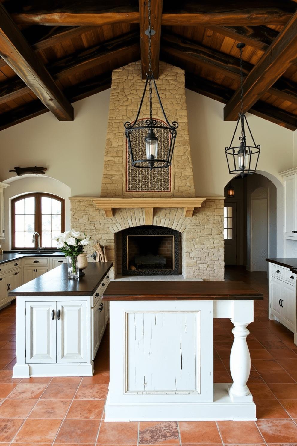 A stunning Mediterranean kitchen featuring a stone fireplace as the focal point. The fireplace is adorned with intricate tile work and rustic wooden beams overhead, creating a warm and inviting atmosphere. The kitchen is spacious with terracotta tiles on the floor and whitewashed cabinetry. A large island with a dark wood countertop provides ample space for cooking and entertaining, complemented by wrought iron pendant lights above.