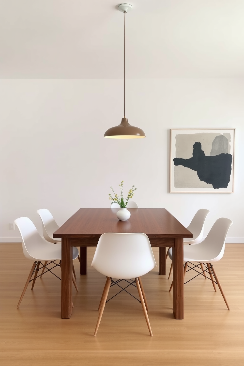 A minimalist dining room features a sleek wooden table paired with simple white chairs. Above the table, an elegant pendant light serves as the focal point, casting a warm glow over the space. The walls are painted in a soft neutral tone, enhancing the room's airy feel. A large abstract artwork hangs on one wall, adding a touch of sophistication to the minimalist aesthetic.