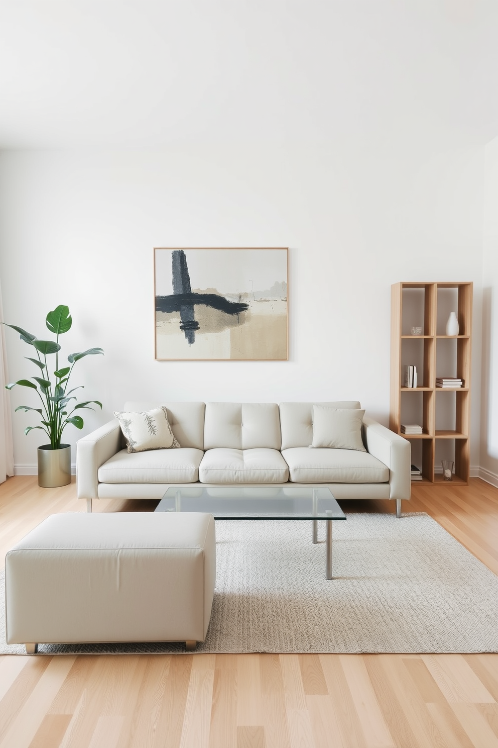 A minimalist living room featuring a sleek low-profile sofa in a neutral color, complemented by a simple glass coffee table in the center. The walls are painted white, and a large abstract artwork hangs above the sofa, adding a touch of color without overwhelming the space. In one corner, a tall indoor plant adds a natural element, while a minimalist bookshelf against the opposite wall showcases a few carefully selected decorative items. The floor is finished with light hardwood, and a soft area rug anchors the seating area, providing warmth and comfort.