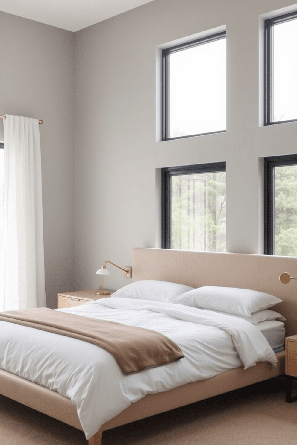 A sleek minimalist bedroom features a low-profile bed with a soft beige upholstered headboard and crisp white linens. The furniture includes a simple nightstand with a small lamp and a minimalist dresser, all in light wood tones. Large windows allow natural light to flood the space, with sheer white curtains gently framing the view. The walls are painted in a soft gray, creating a calming atmosphere that complements the neutral color palette.