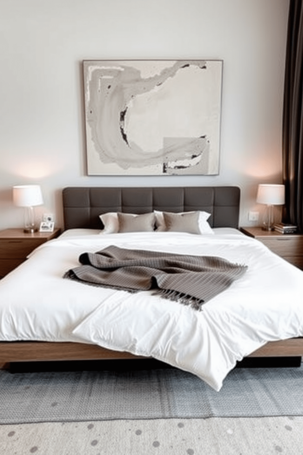 A modern bedroom features a sleek platform bed with a low profile and clean lines. The bed is dressed in crisp white linens, accented by a textured throw blanket and a few decorative pillows in muted tones. Flanking the bed are minimalist nightstands with simple lamps that provide soft lighting. A large abstract painting hangs above the headboard, adding a touch of color to the neutral palette.