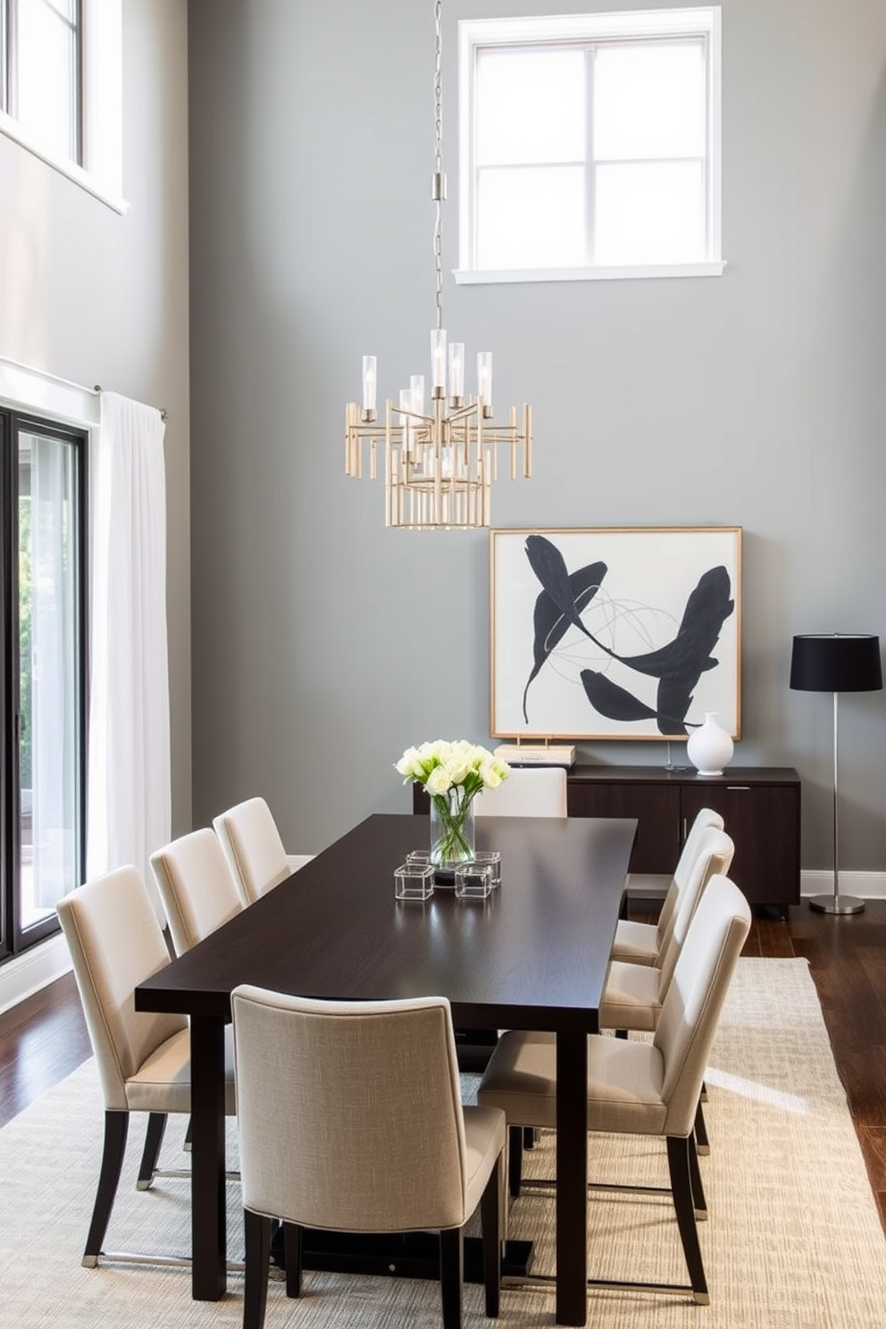 A modern dining room featuring a sleek dark wood table surrounded by light upholstered chairs. The walls are painted in a soft gray, creating a striking contrast with the bold black accent wall adorned with abstract art. Natural light floods the space through large windows, illuminating the minimalist decor. A statement chandelier with metallic finishes hangs above the table, adding elegance and warmth to the room.