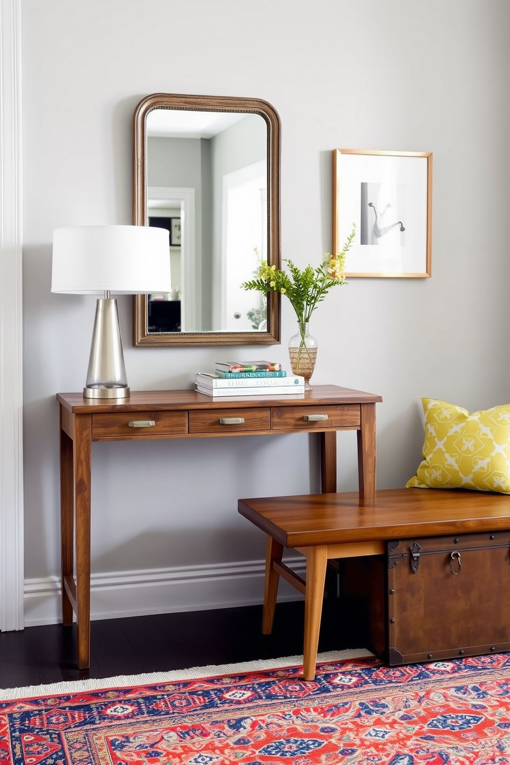 A stylish entryway that combines vintage pieces with modern furnishings. A rustic wooden console table sits against the wall, adorned with a sleek modern lamp and an antique mirror above it. To the side, a contemporary bench with clean lines contrasts with a vintage trunk used for storage. The walls are painted a soft gray, and a vibrant area rug adds warmth and color to the space.