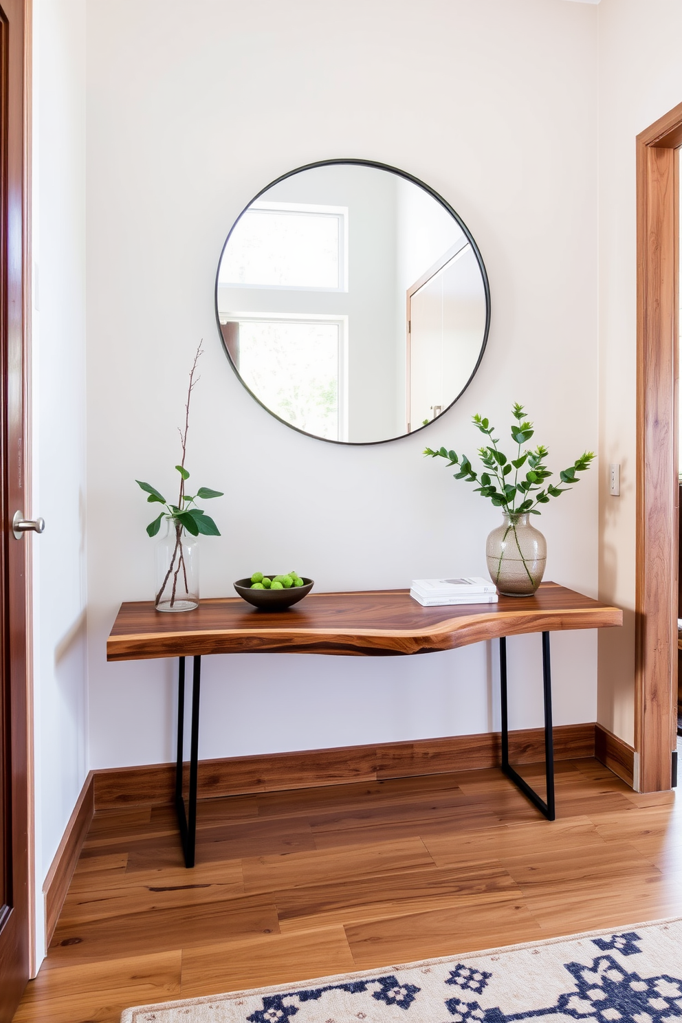 A modern entryway featuring natural wood accents that add warmth and texture. The space includes a sleek console table with a live edge wood top and minimalist metal legs. A large round mirror is mounted above the table, reflecting natural light from a nearby window. The floor is adorned with a stylish area rug that complements the wood tones and adds a cozy feel.