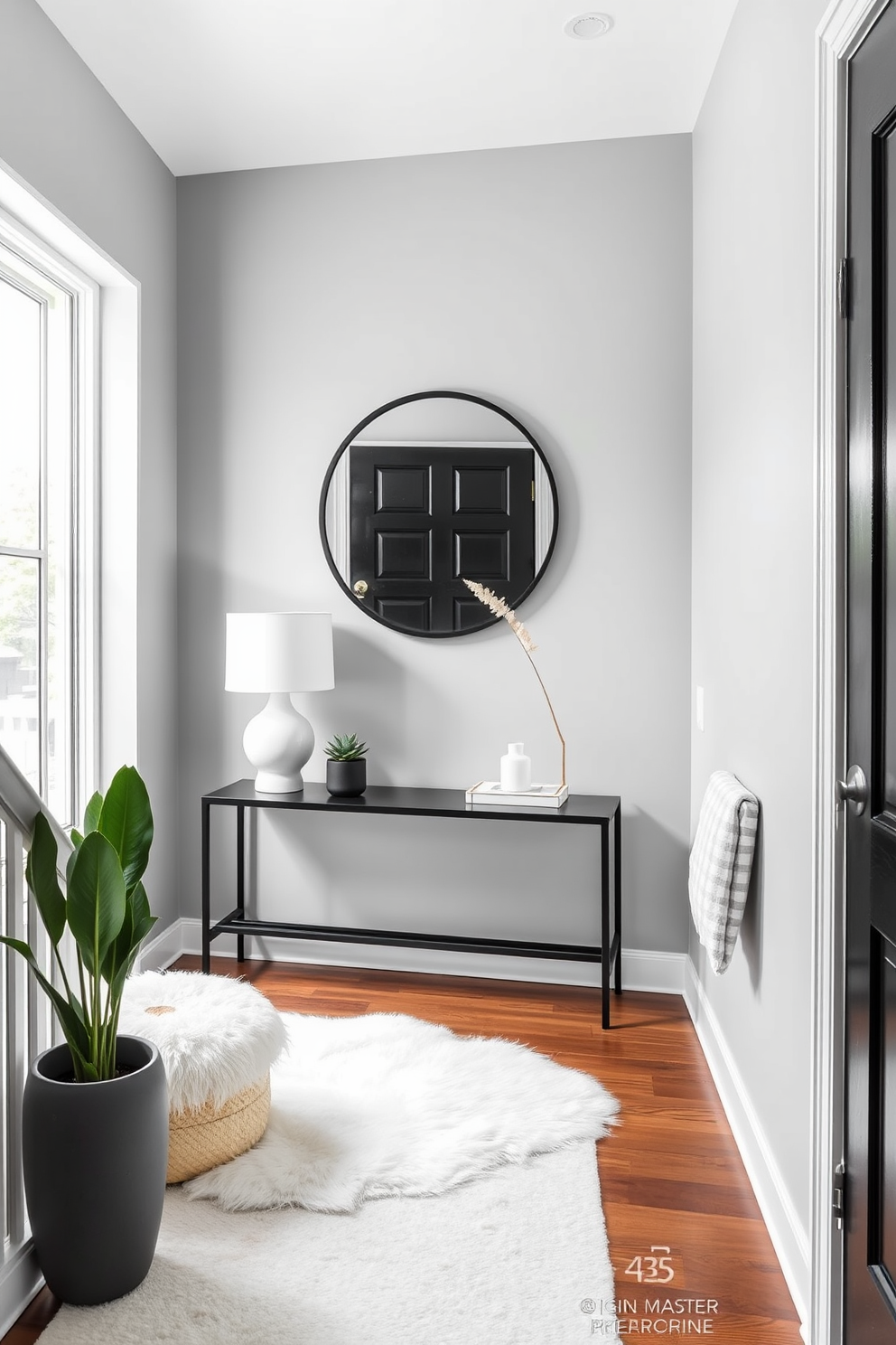 A sleek modern entryway featuring a monochrome color palette. The walls are painted in a soft gray, complemented by a black console table adorned with a minimalist lamp and a small potted plant. The floor is covered with a plush white rug that adds warmth to the space. A large round mirror with a black frame hangs above the console, reflecting natural light from a nearby window.