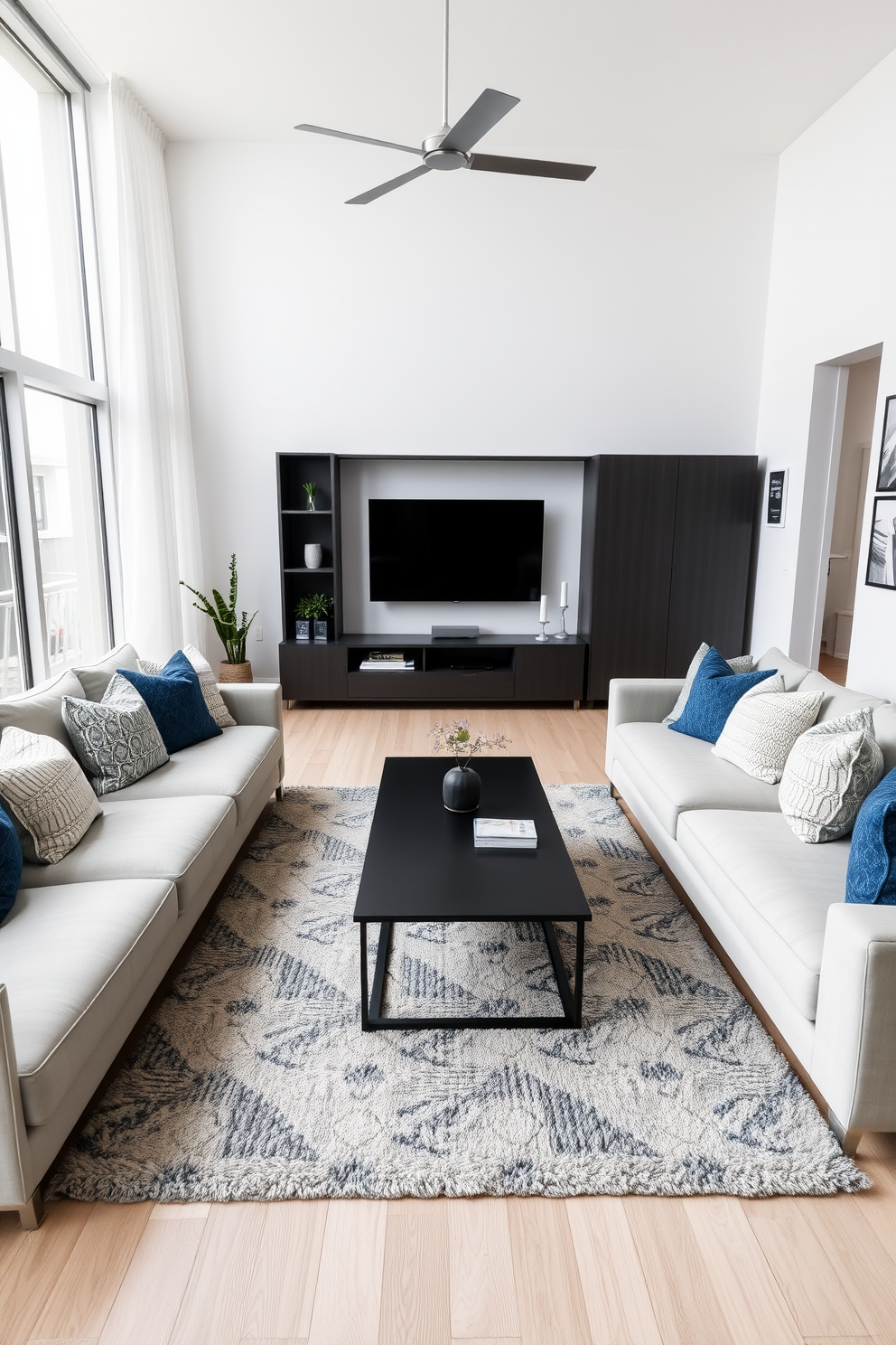 A modern family room featuring a large sectional sofa adorned with textured throw pillows in various shades of blue and gray. The walls are painted a soft white, and a sleek coffee table sits in the center, complemented by a cozy area rug that adds warmth to the space. Floor-to-ceiling windows allow natural light to flood the room, highlighting the minimalist decor. A stylish entertainment unit houses a flat-screen TV, while a few decorative plants bring a touch of nature indoors.