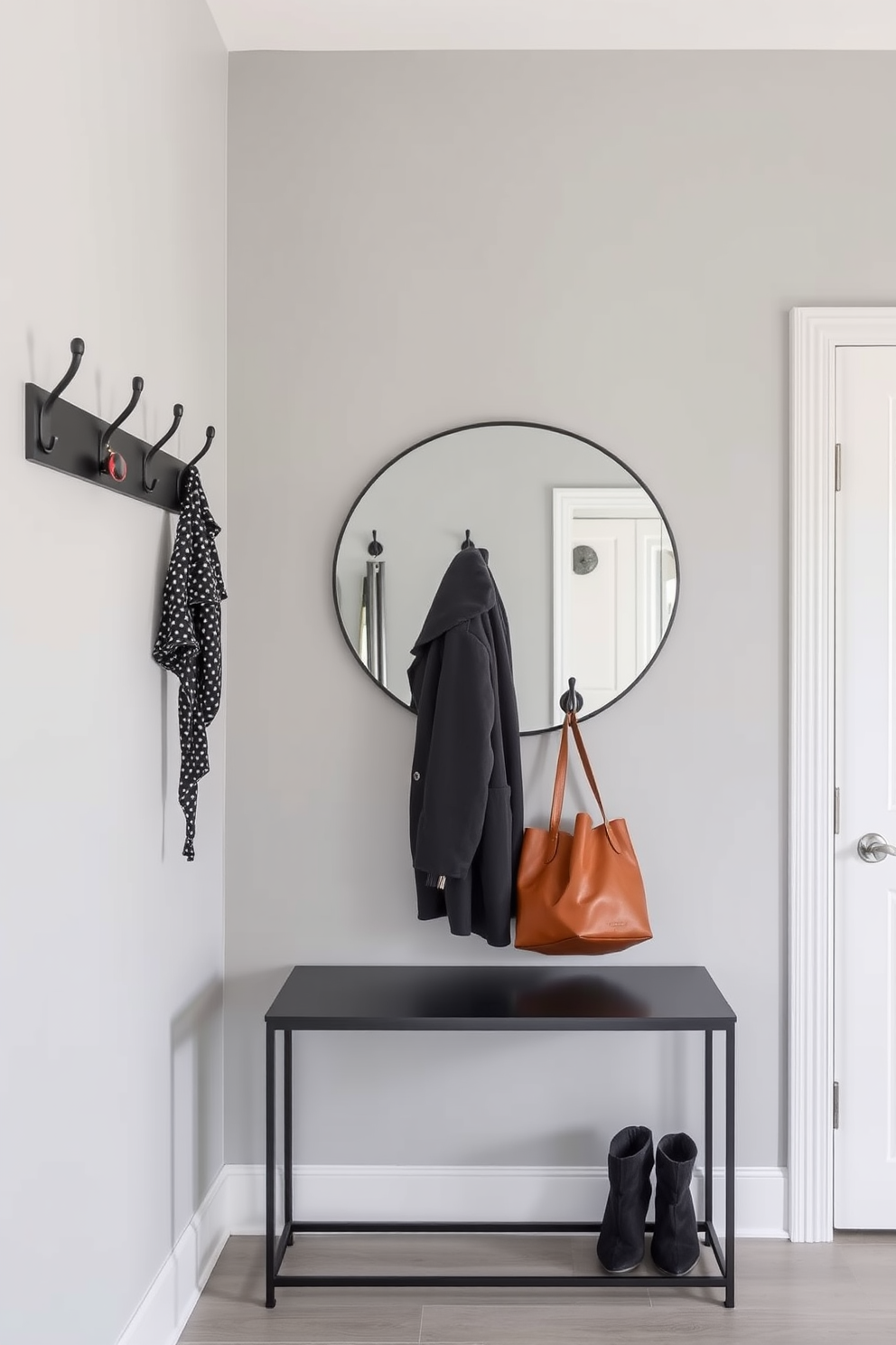 A modern foyer featuring functional hooks for coats and bags. The walls are painted in a soft gray with a sleek console table below a large round mirror.