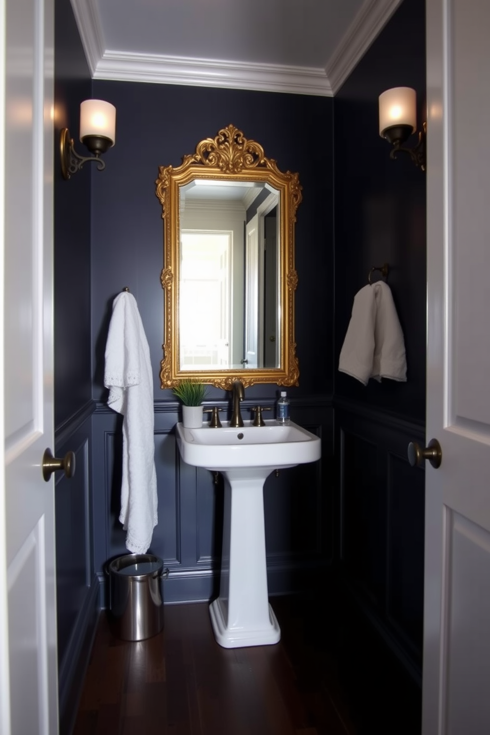 A moody powder room featuring dimmable sconces that create an inviting ambiance. The walls are painted in a deep navy blue, and the floor is adorned with dark wood planks for a warm touch. A sleek pedestal sink is complemented by a vintage gold-framed mirror above it. Decorative elements such as a small potted plant and a luxurious hand towel add a sophisticated finish to the space.