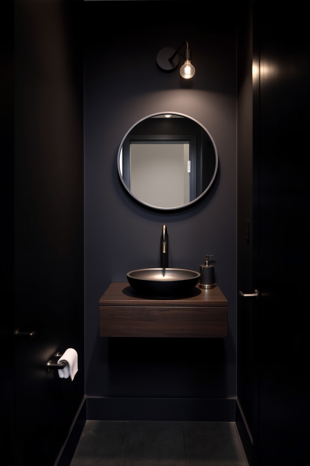 A moody powder room featuring deep charcoal walls that create an intimate atmosphere. The space is accented with matte black fixtures, including a sleek faucet and a minimalist wall-mounted light. A stylish floating vanity made of dark wood complements the overall design. A round mirror with a thin black frame hangs above the vanity, enhancing the modern aesthetic.