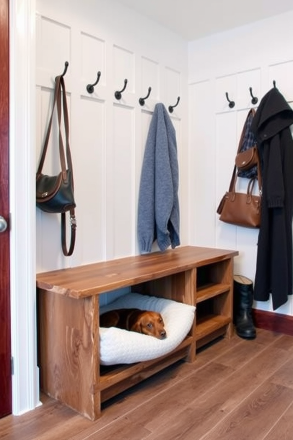 A stylish mudroom features a sleek bench with a cozy integrated pet bed underneath, providing a perfect spot for your furry friend. The bench is crafted from reclaimed wood, and the surrounding walls are adorned with hooks for coats and bags, creating a functional yet inviting space.