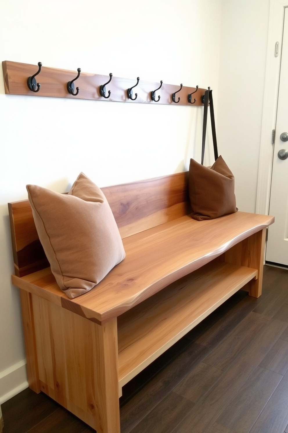 A rustic bench with a live edge design made from reclaimed wood sits against the wall. The bench features a natural finish that highlights the wood grain and is complemented by cozy throw pillows in earthy tones. In the mudroom, the bench provides a practical seating area for removing shoes and storing outdoor gear. Above the bench, hooks are mounted on the wall for hanging coats and bags, enhancing the functionality of the space.