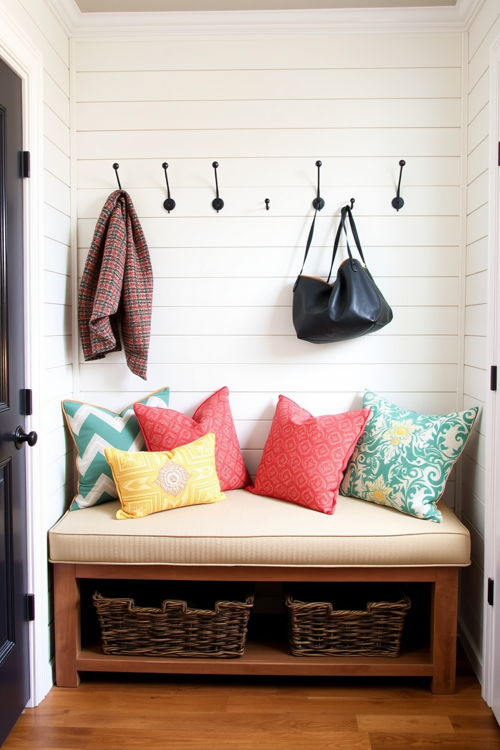 A cozy mudroom featuring an upholstered bench adorned with colorful cushions. The bench is positioned against a backdrop of shiplap walls painted in a soft white hue, with hooks above for hanging coats and bags.