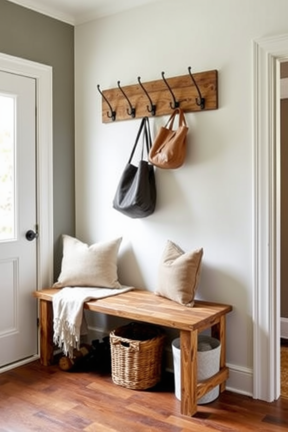 A stylish mudroom features a ladder-style bench made of reclaimed wood, adding a rustic charm to the space. Above the bench, hooks are mounted on the wall for coats and bags, while a woven basket sits underneath for storage. The bench is complemented by a soft cushion in a neutral fabric, providing comfort and style. Natural light floods the room through a nearby window, highlighting the earthy tones of the decor.