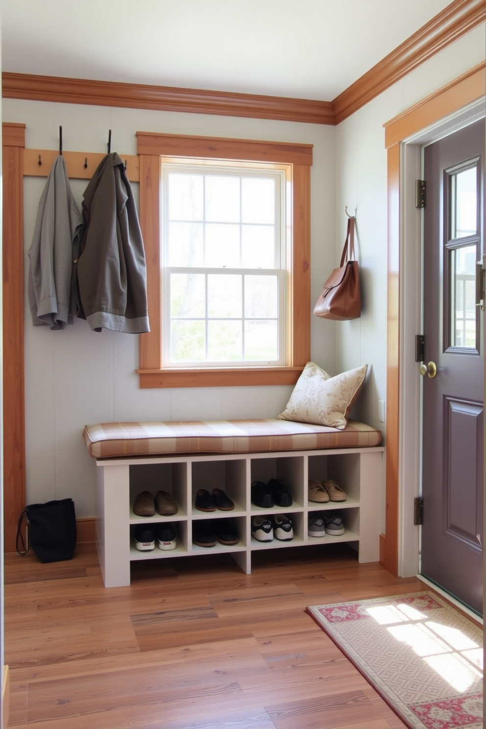 A functional bench with shoe storage is positioned against the wall, featuring a cushioned seat for comfort. Below the bench, multiple compartments neatly organize shoes, while hooks above provide space for coats and bags. The mudroom is designed with a blend of practicality and style, incorporating a light color palette to create an inviting atmosphere. Natural light floods the space through a nearby window, enhancing the warm wooden accents and decorative elements.