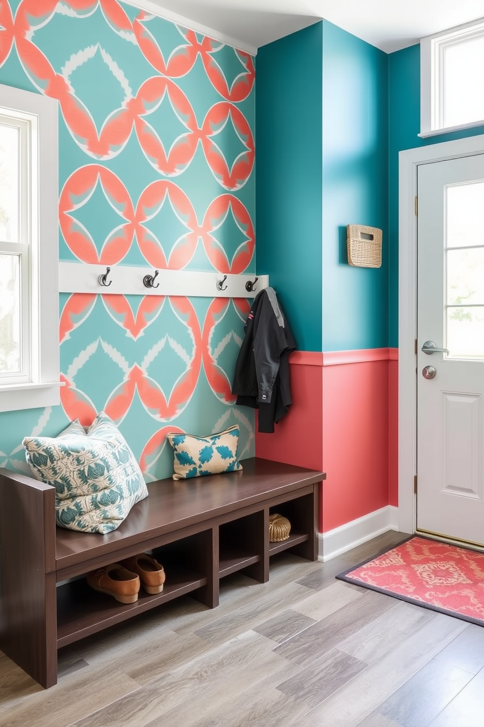 A vibrant accent wall featuring a bold geometric pattern in shades of teal and coral adds personality to the space. The wall is complemented by a sleek bench with built-in storage and hooks for hanging coats and bags. The mudroom is designed with a practical layout, incorporating durable flooring that withstands heavy foot traffic. Natural light floods the area through a large window, enhancing the welcoming atmosphere.