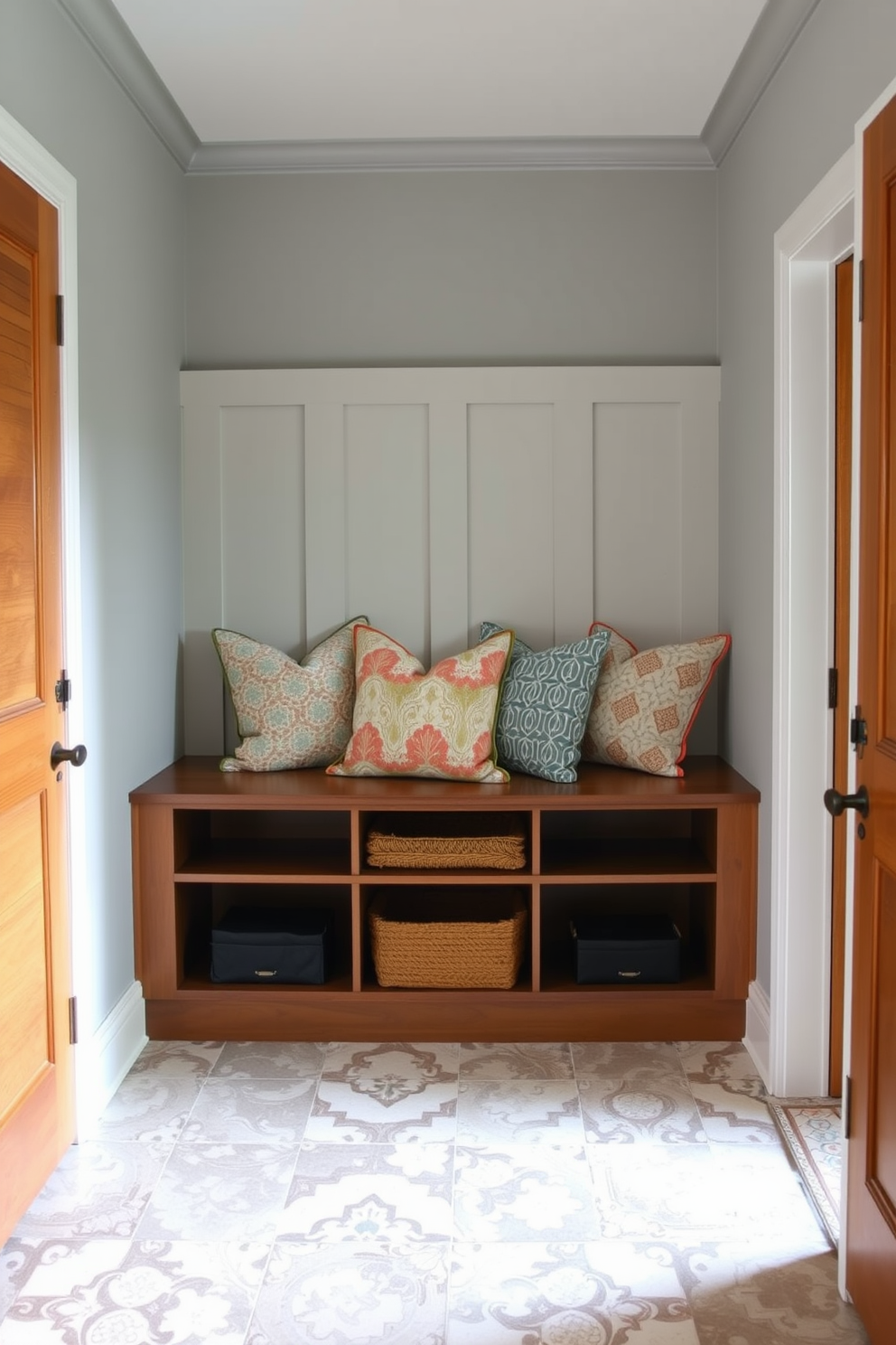 A welcoming mudroom features a built-in wooden bench adorned with soft, colorful cushions for comfort. The walls are painted in a light gray tone, while the floor showcases durable, patterned tiles that add visual interest.