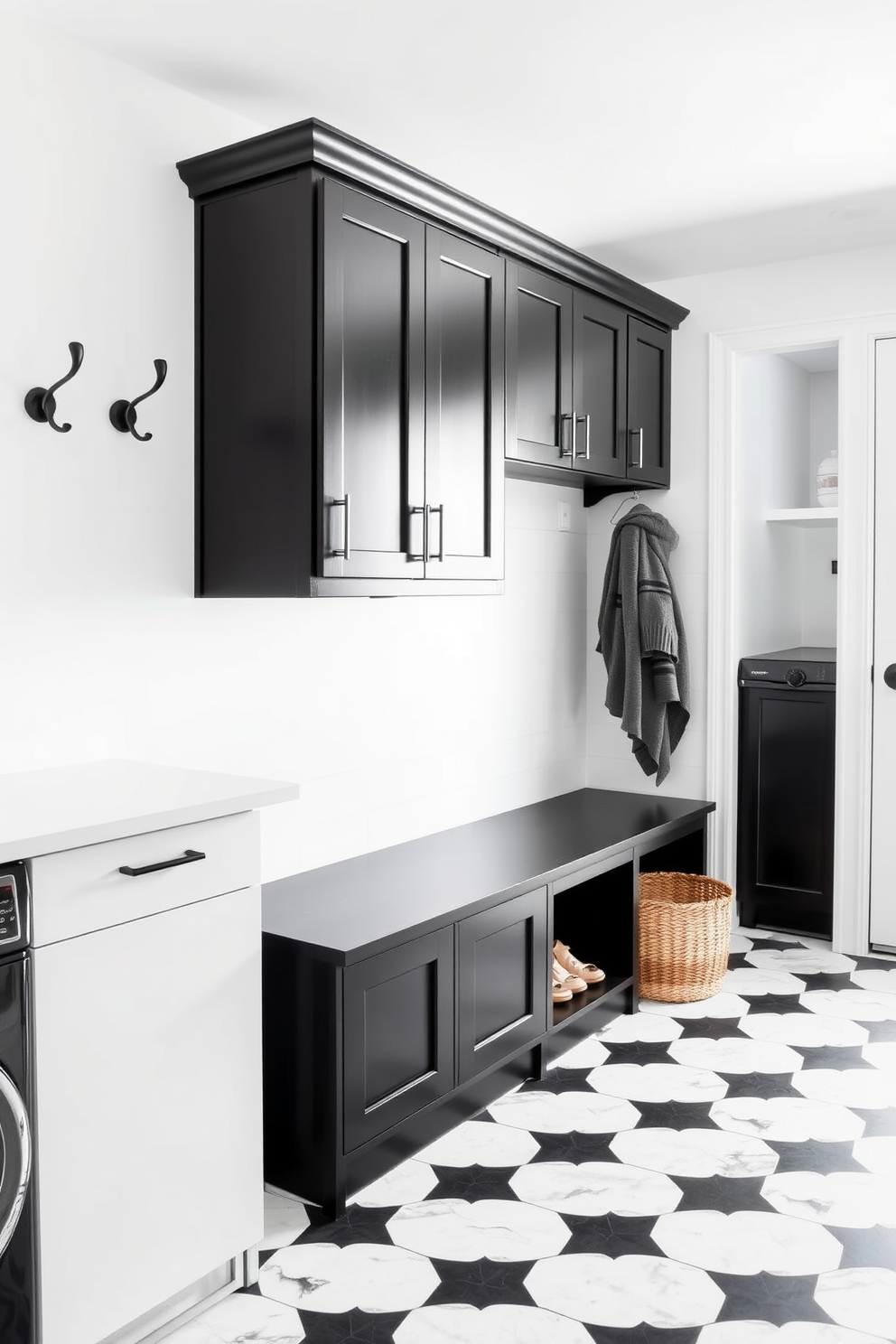 A contemporary mudroom laundry room features sleek black cabinetry paired with white countertops. The walls are painted in a crisp white, creating a bright and airy atmosphere, while a stylish black bench with storage underneath provides functionality. The floor is adorned with large black and white tiles that add a modern touch. A row of hooks in black metal is mounted on the wall for hanging coats, and a woven basket sits on the floor for shoes.