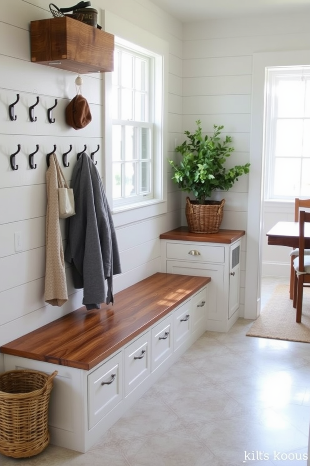 A charming mudroom features a large farmhouse sink with a rustic wooden countertop. The walls are adorned with shiplap, and a row of hooks hangs above a bench for easy storage of coats and bags. Adjacent to the dining room, the mudroom incorporates a stylish tile floor that complements the dining area. Natural light floods in through a window, illuminating a decorative basket filled with fresh greenery.