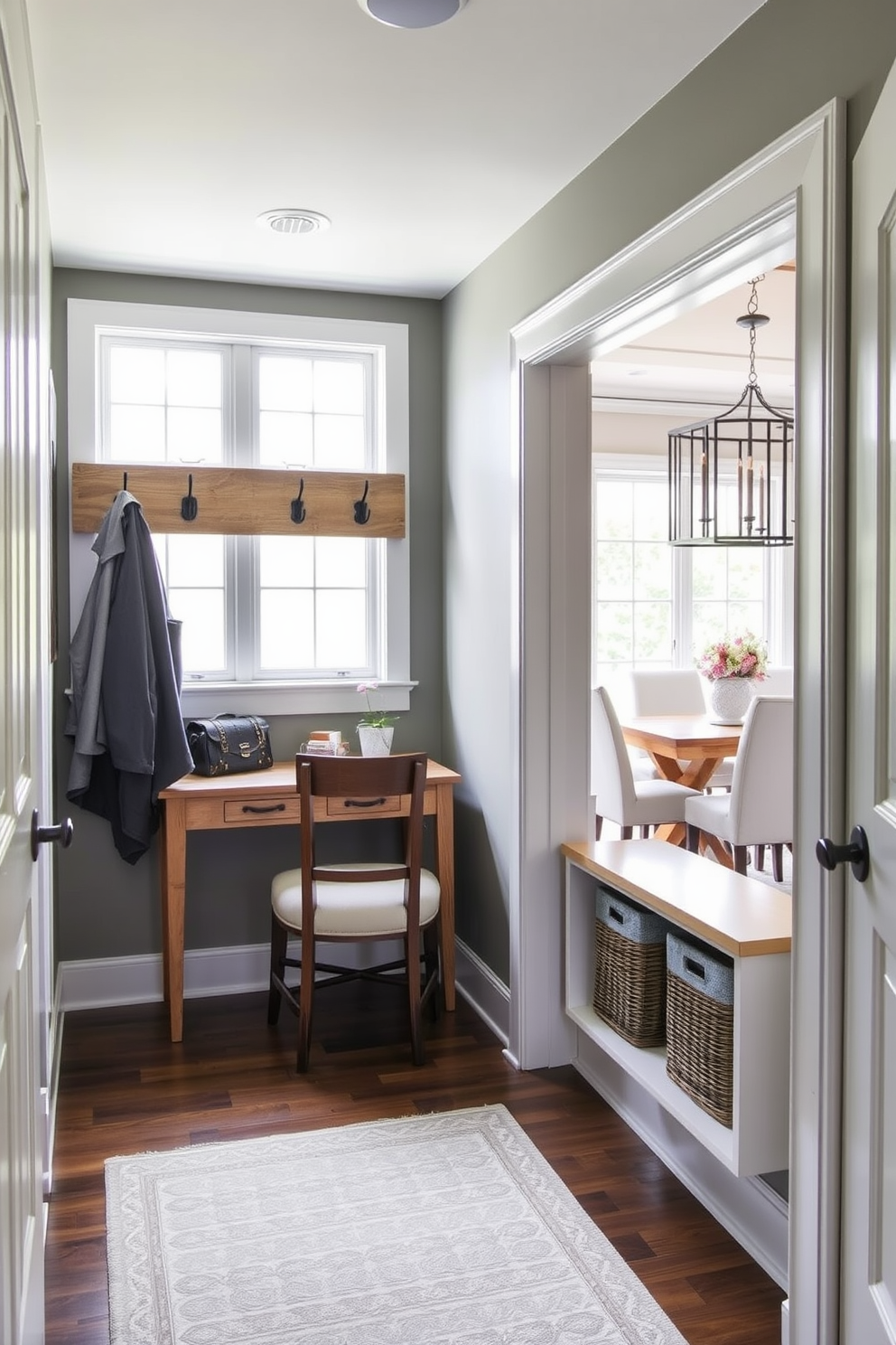 A stylish mudroom with a small desk area. The desk is made of reclaimed wood and features a comfortable chair, with hooks above for coats and bags. The walls are painted in a soft gray tone, complemented by a patterned area rug on the floor. A large window allows natural light to fill the space, creating an inviting atmosphere. Adjacent to the dining room, the mudroom has easy access to both spaces. Decorative baskets are placed on a shelf for storage, adding to the functional yet aesthetic design.