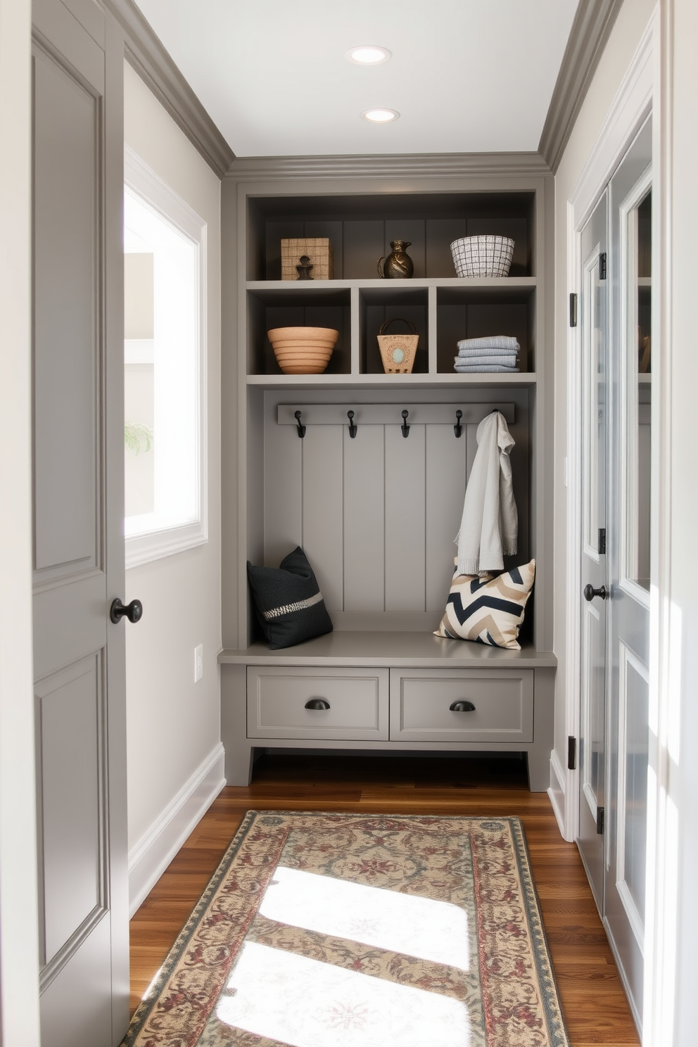 A stylish mudroom features a small laundry nook seamlessly integrated into the design. The space includes built-in cabinetry with open shelving for storage and a bench for seating, all finished in a soft gray tone. Adjacent to the family room, the mudroom offers easy access while maintaining a cohesive aesthetic. Natural light floods the area through a nearby window, highlighting decorative hooks and a patterned area rug that adds warmth to the space.