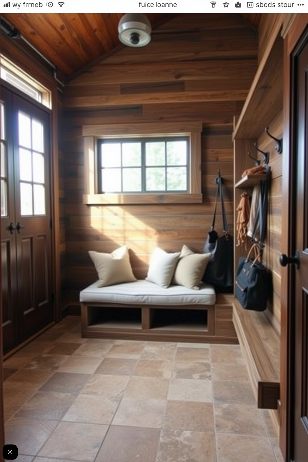 A cozy mudroom near the garage features rustic wood accents that create a warm and inviting atmosphere. The space includes a built-in bench with plush cushions, surrounded by wooden hooks for hanging coats and bags. Natural light floods the room through a large window, illuminating the reclaimed wood paneling on the walls. A durable tile floor with earthy tones complements the wooden elements, enhancing the rustic charm of the design.