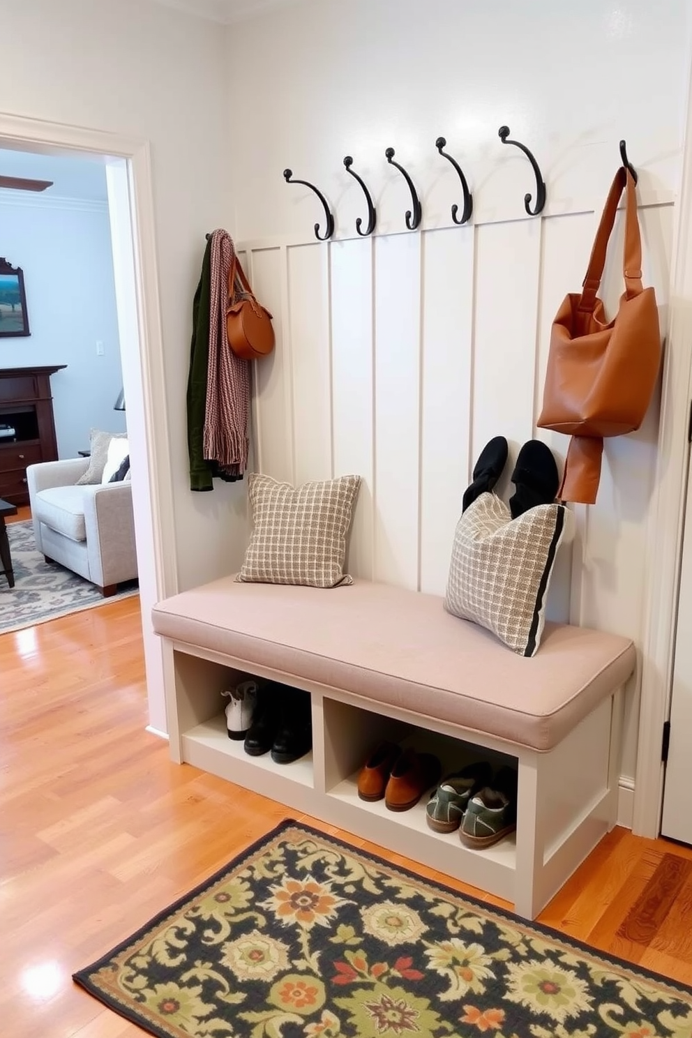 Cozy bench with storage underneath in a mudroom near the living room. The bench is upholstered in a soft fabric, providing a comfortable seating area, while the storage compartment below is perfect for shoes and outdoor gear. The mudroom features light-colored walls and a warm wood floor, creating an inviting atmosphere. Decorative hooks line the wall above the bench, ideal for hanging coats and bags, complemented by a stylish area rug that adds a pop of color.