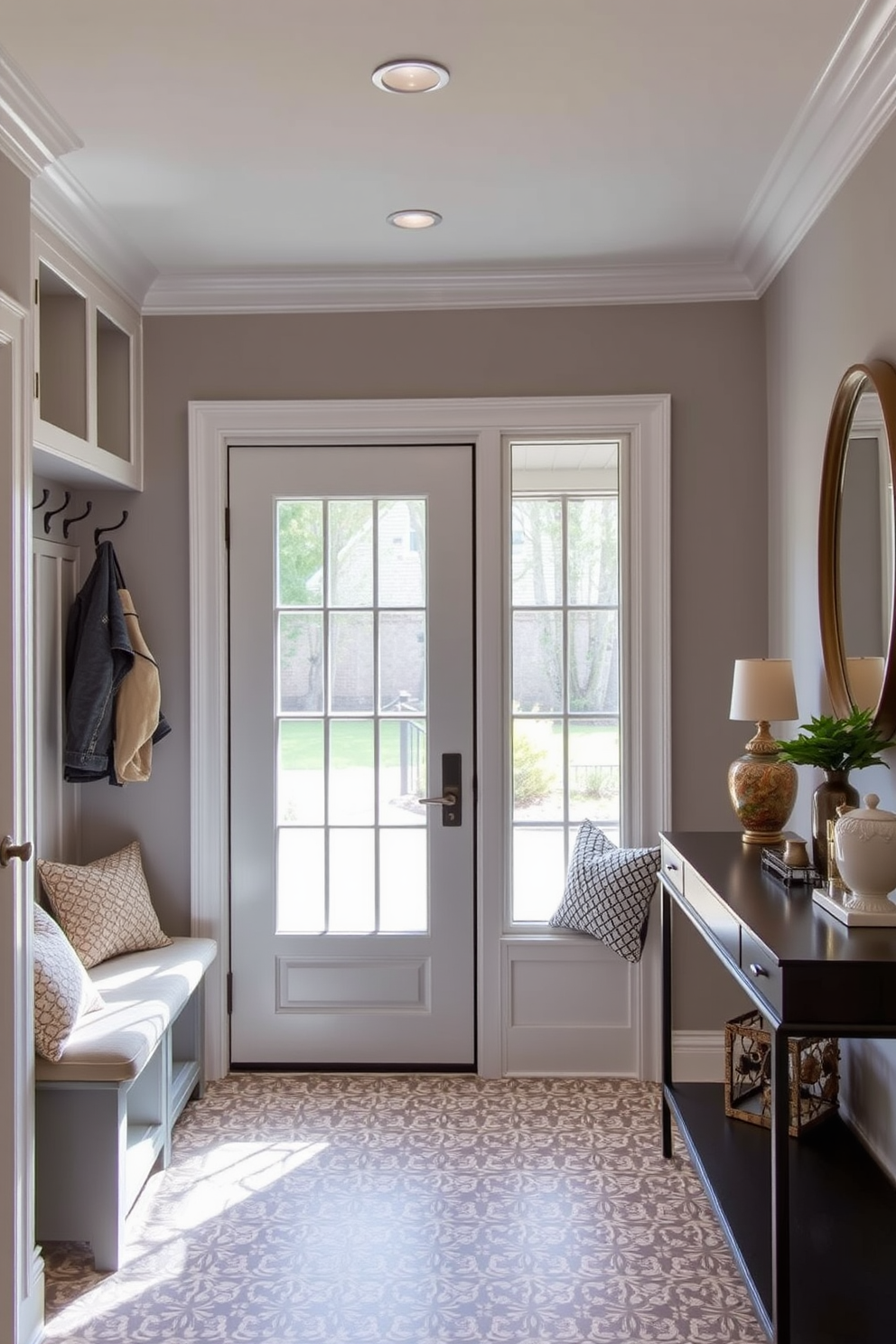 A bright and inviting mudroom features a large glass door that allows natural light to flood the space. The walls are painted in a soft gray, and the floor is adorned with patterned tiles that add a touch of elegance. Built-in benches with plush cushions provide a comfortable seating area, while hooks above offer convenient storage for coats and bags. To the right, a stylish console table holds decorative items and a small potted plant, enhancing the room's welcoming atmosphere.