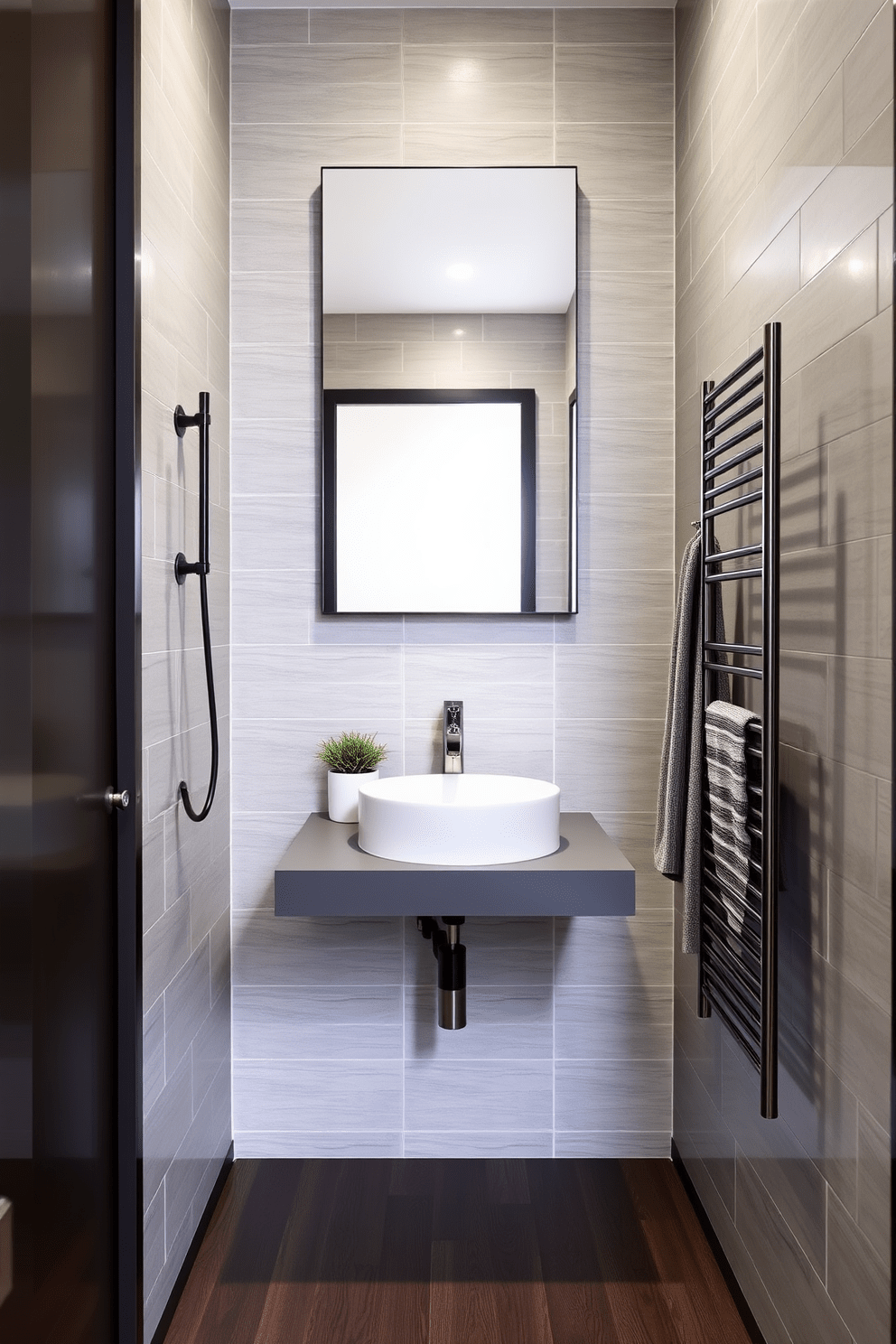 A narrow bathroom design featuring wall-mounted faucets to maximize space efficiency. The walls are adorned with light gray tiles and a sleek, floating vanity with a white sink sits beneath a large mirror. The floor is covered in dark wood planks, adding warmth to the compact area. A small potted plant is placed on the vanity, and a stylish towel rack is mounted on the wall beside the sink.