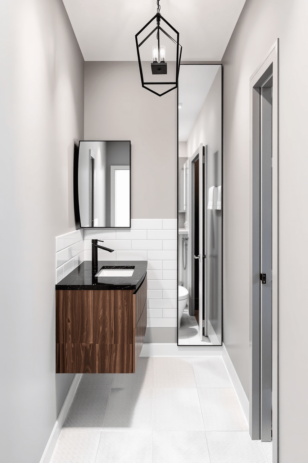 A narrow bathroom design featuring a sleek, elongated layout. The walls are painted in a soft gray tone, complemented by white subway tiles that create a clean and modern aesthetic. A floating vanity with a dark wood finish is positioned against one wall, topped with a striking black granite countertop. Above the vanity, a unique geometric light fixture with a matte black finish adds character and a contemporary touch. On the opposite wall, a tall mirror stretches from the countertop to the ceiling, enhancing the sense of space. The floor is adorned with light-colored, textured tiles that provide a subtle contrast to the walls.