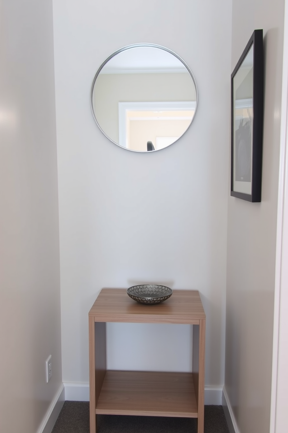 A small side table for keys and mail is positioned against the wall in a narrow entryway. The table features a sleek design with a light wood finish and a lower shelf for additional storage. Above the table, a round mirror with a minimalist frame reflects the space, enhancing the sense of openness. A small decorative bowl sits on the table, providing a stylish catch-all for everyday items.