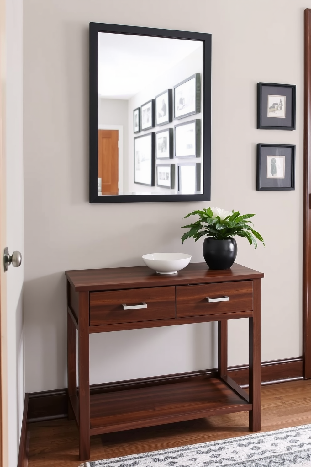 A compact console table with drawers sits elegantly against the wall in a narrow entryway. The table is finished in a rich walnut stain, complementing a stylish wall mirror that enhances the sense of space. Above the console, a series of framed artwork adds a personal touch while maintaining a cohesive color palette. A small decorative bowl and a fresh potted plant are placed on the table, creating a welcoming atmosphere.