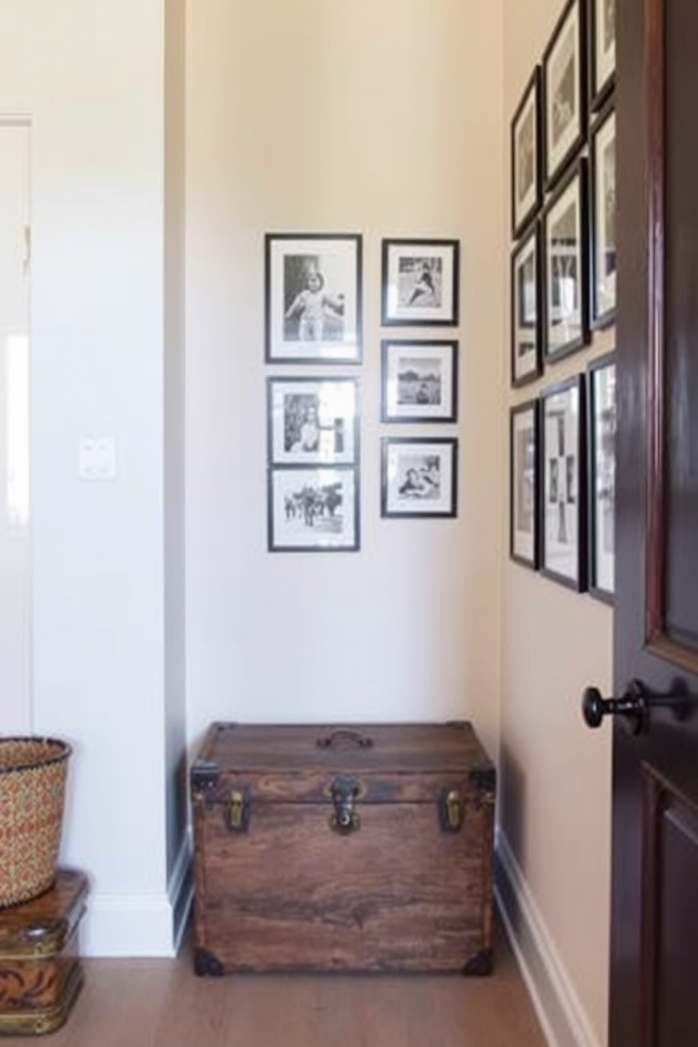 A narrow entryway features a vintage trunk used as a stylish storage solution. The walls are adorned with soft pastel colors and a gallery of framed black and white photographs.