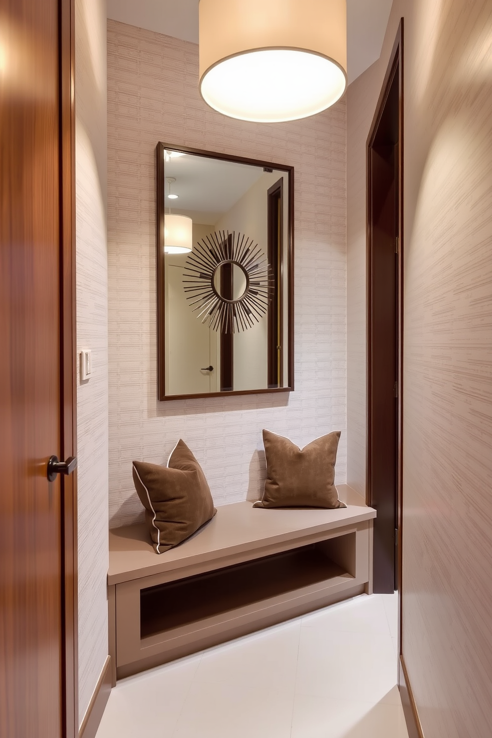 A narrow foyer features sleek built-in under-bench storage that blends seamlessly with the wall. The space is illuminated by a stylish pendant light, enhancing the warm tones of the wood finishes. The walls are adorned with subtle wallpaper that adds texture without overwhelming the small area. A decorative mirror above the bench creates an illusion of depth, making the foyer feel more spacious.