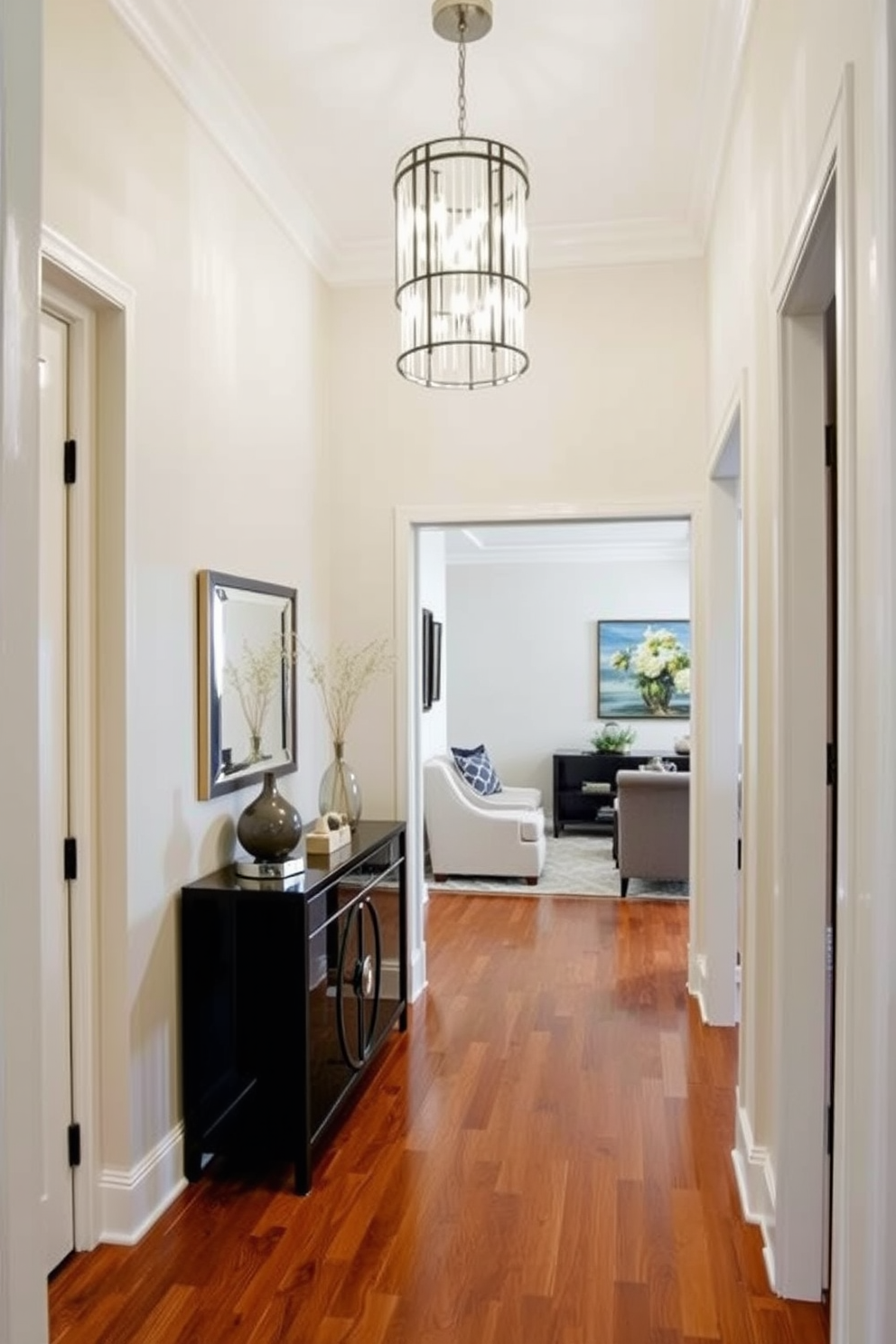 A narrow foyer with elegant design elements invites guests into the home. The walls are adorned with soft neutral tones, complemented by a statement light fixture that hangs gracefully overhead. A sleek console table is positioned against one wall, topped with decorative accents and a small mirror. The flooring features a rich hardwood finish, enhancing the warmth of the space while guiding visitors into the main living areas.