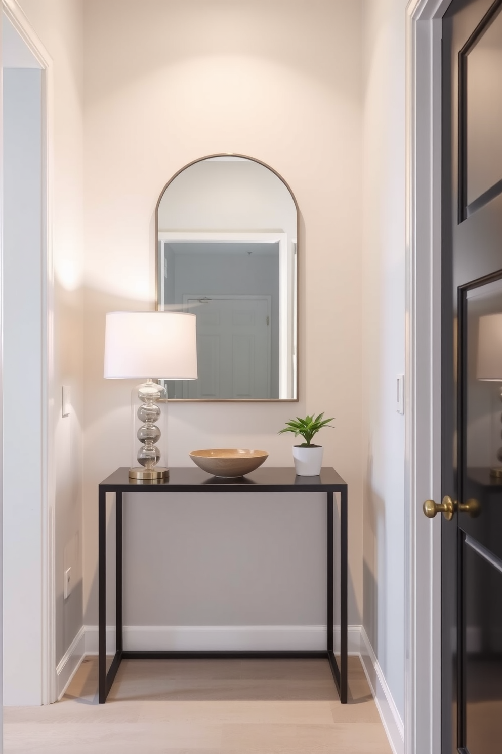 A narrow foyer features a sleek console table against the wall, topped with a stylish lamp and a decorative bowl. A wall-mounted mirror above the console reflects light and adds depth, while a small potted plant sits on the table to bring a touch of greenery.