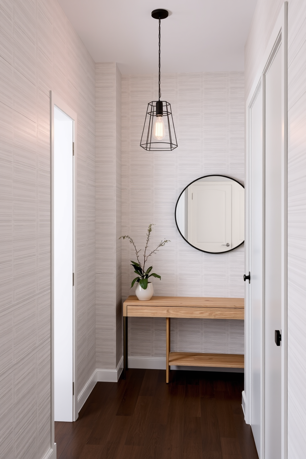 A narrow foyer design featuring a cohesive color palette of soft greys and warm whites. The walls are adorned with subtle textured wallpaper, while a sleek console table in a light wood finish stands against one side. On the opposite wall, a large round mirror with a thin black frame reflects natural light, enhancing the space. A stylish pendant light hangs from the ceiling, providing a warm glow, and a small potted plant adds a touch of greenery to the scene.