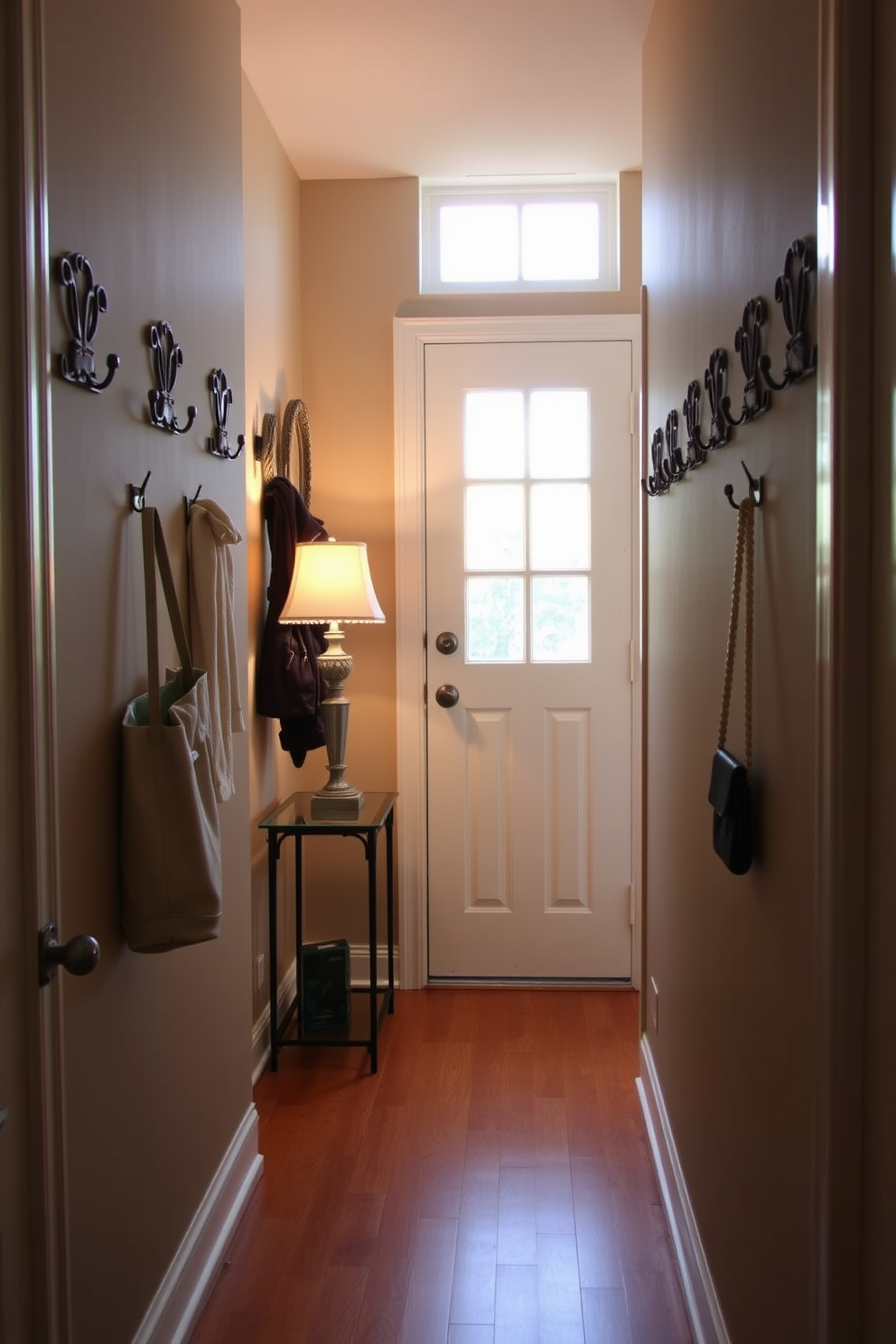 A narrow foyer features decorative hooks mounted on the wall for coats and bags, creating an inviting and organized entryway. The flooring is a warm hardwood, complemented by a small console table adorned with a stylish lamp and a decorative mirror above.