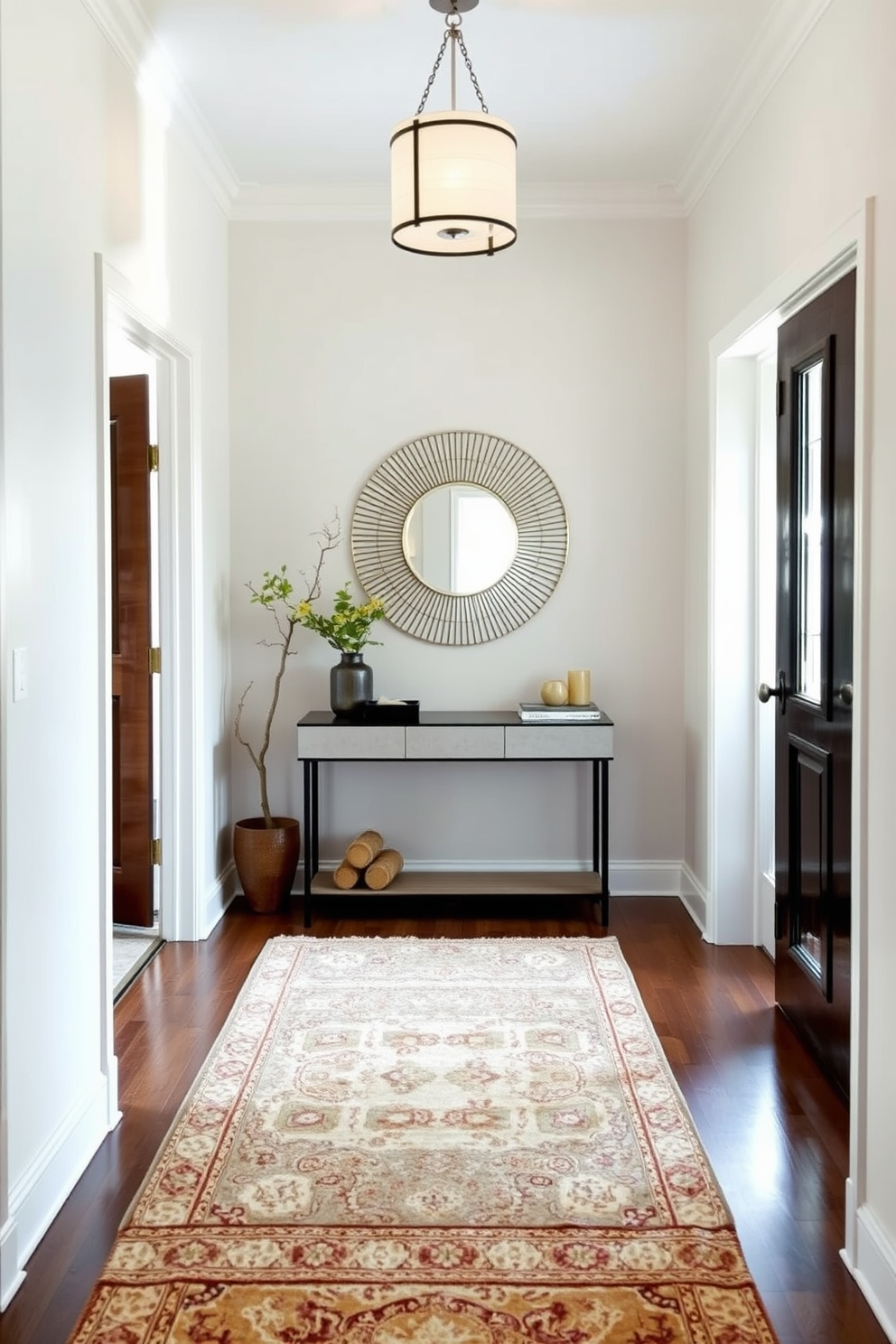 A narrow foyer featuring layered rugs that add texture and warmth. The space is illuminated by a stylish pendant light, and a sleek console table is positioned against the wall. The walls are painted in a soft neutral tone, creating a welcoming atmosphere. A decorative mirror hangs above the console, reflecting the natural light from a nearby window.