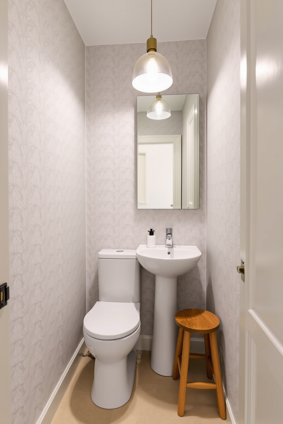 A narrow powder room featuring a sleek, modern toilet and a compact pedestal sink. The walls are adorned with a soft, light gray wallpaper and a large mirror above the sink reflects the space, enhancing its openness. In one corner, a small wooden stool provides additional seating while complementing the overall decor. A stylish pendant light hangs from the ceiling, casting a warm glow over the room and highlighting the elegant fixtures.