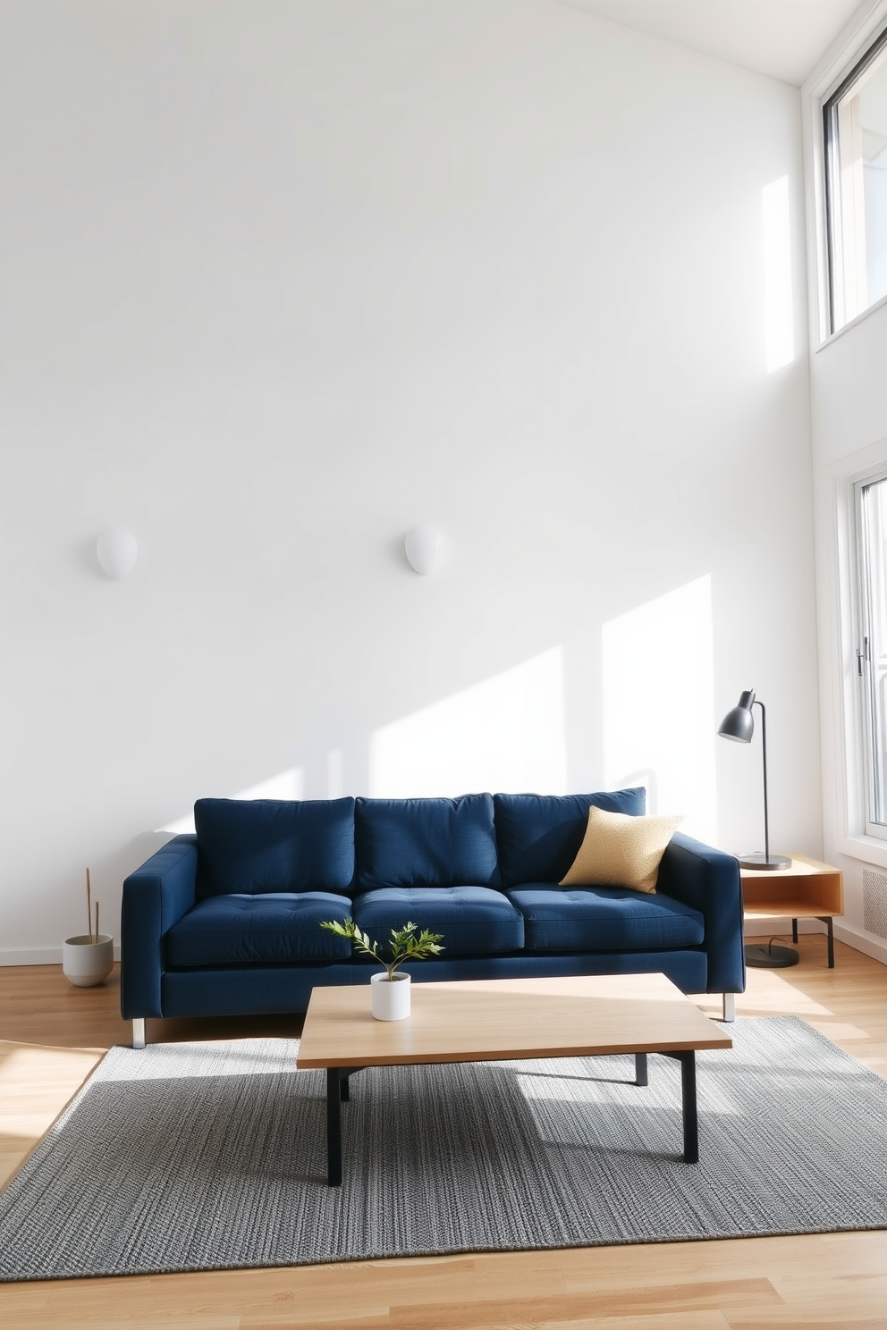 A navy blue couch is the focal point of a minimalist living room, set against a crisp white wall. The surrounding decor features a light wood coffee table and a textured area rug, creating a cozy yet modern atmosphere. Natural light floods the space through large windows, highlighting the clean lines and simplicity of the design. A few carefully chosen accessories, like a single plant and a minimalist lamp, enhance the overall aesthetic without overwhelming the room.