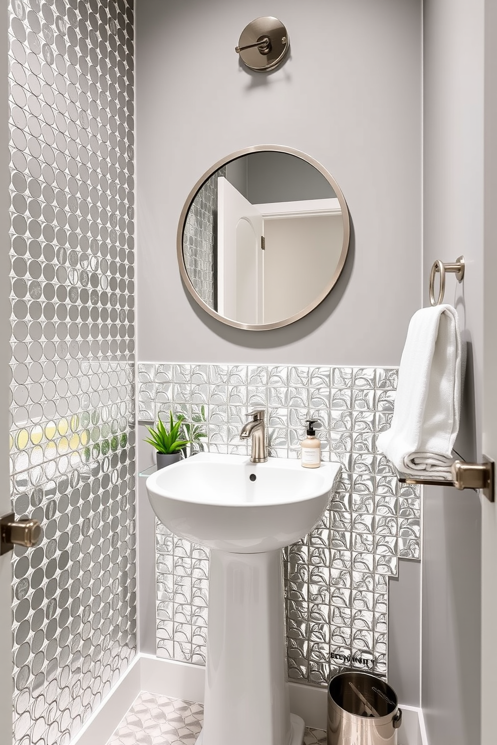 A chic powder room featuring metallic tiles that reflect light and add a contemporary edge. The walls are painted in a soft gray, enhancing the sleek look of the space. A stylish pedestal sink is centered against the wall, complemented by a large round mirror with a brushed metal frame. Decorative accents include a small potted plant and a set of elegant hand towels neatly arranged on a floating shelf.