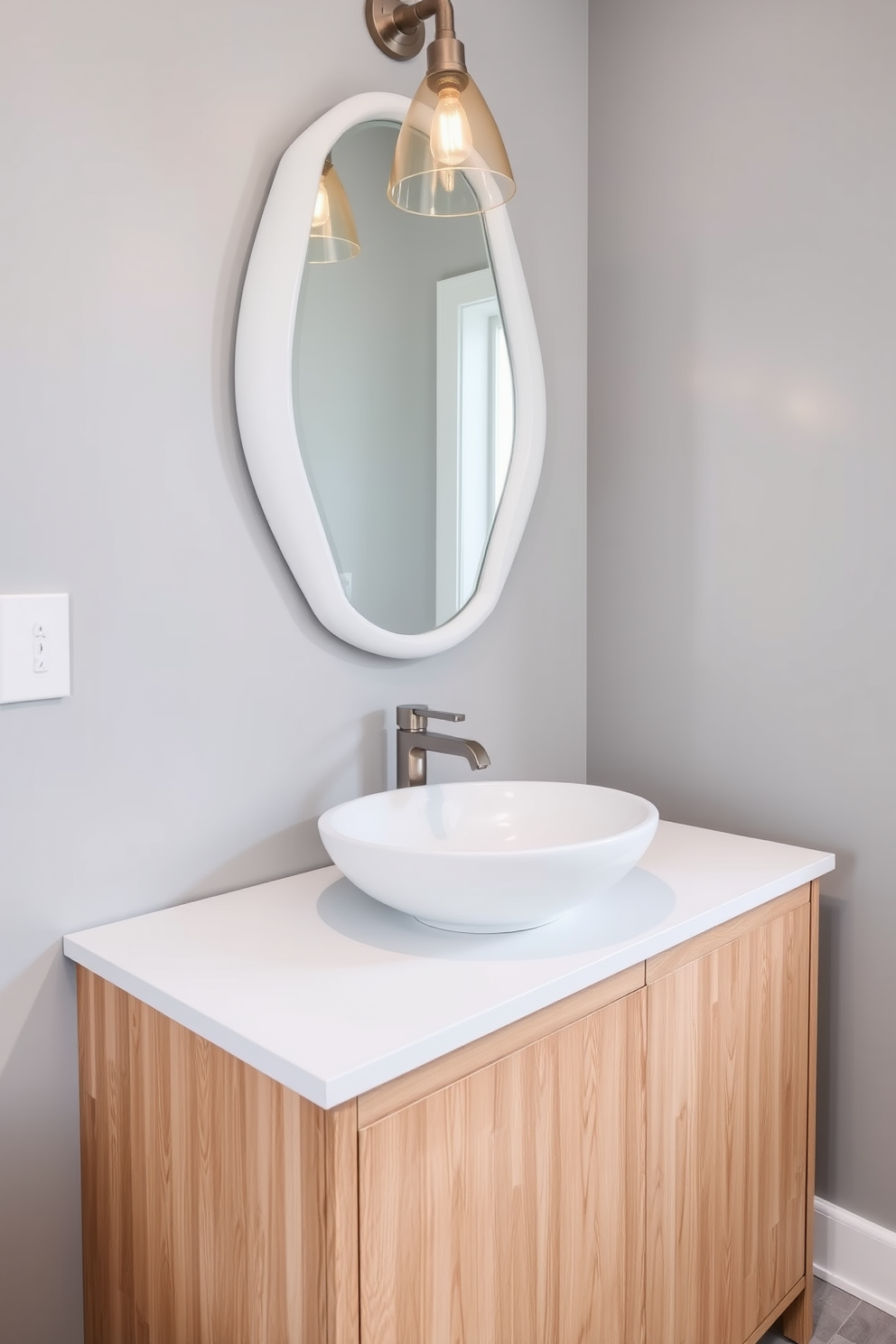 An elegant vessel sink rests atop a sleek white countertop in a stylish powder room. The sink is complemented by a modern faucet in brushed nickel, creating a chic focal point against the backdrop of soft gray walls. Surrounding the sink, a minimalist vanity offers ample storage with clean lines and a natural wood finish. A decorative mirror with a unique shape hangs above, reflecting the warm light from a contemporary pendant fixture overhead.