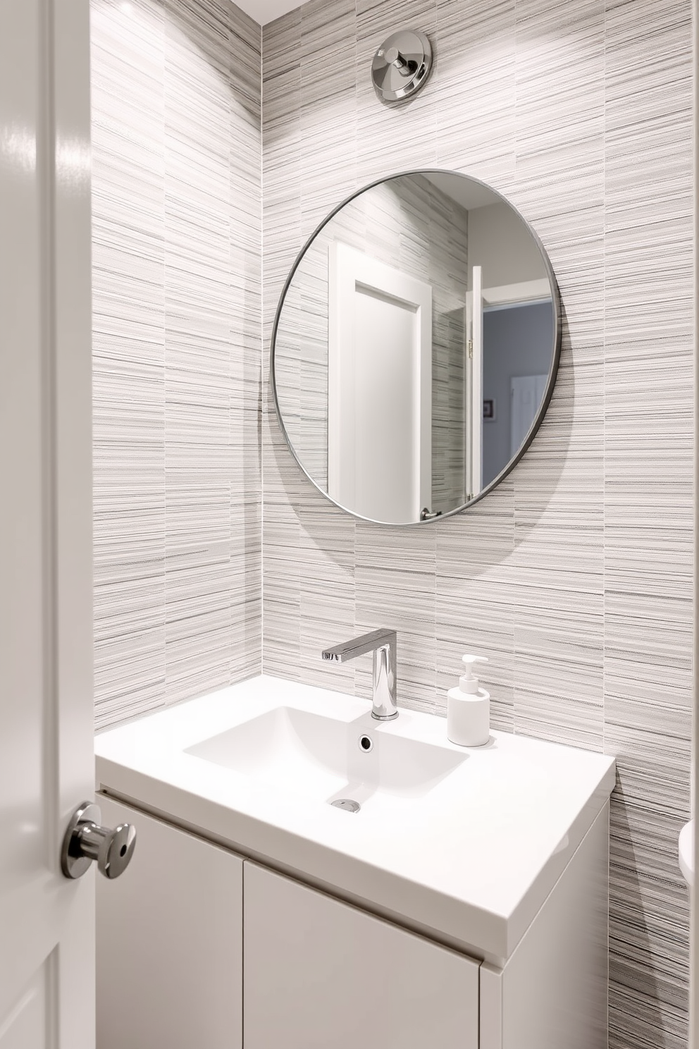 A chic powder room featuring a monochromatic color scheme that exudes elegance. The walls are adorned with textured wallpaper in varying shades of soft gray, complementing the sleek white fixtures. The vanity is a minimalist design with a seamless white countertop and a single elegant sink. Above it, a large round mirror with a thin silver frame reflects the ambient light, enhancing the serene atmosphere.