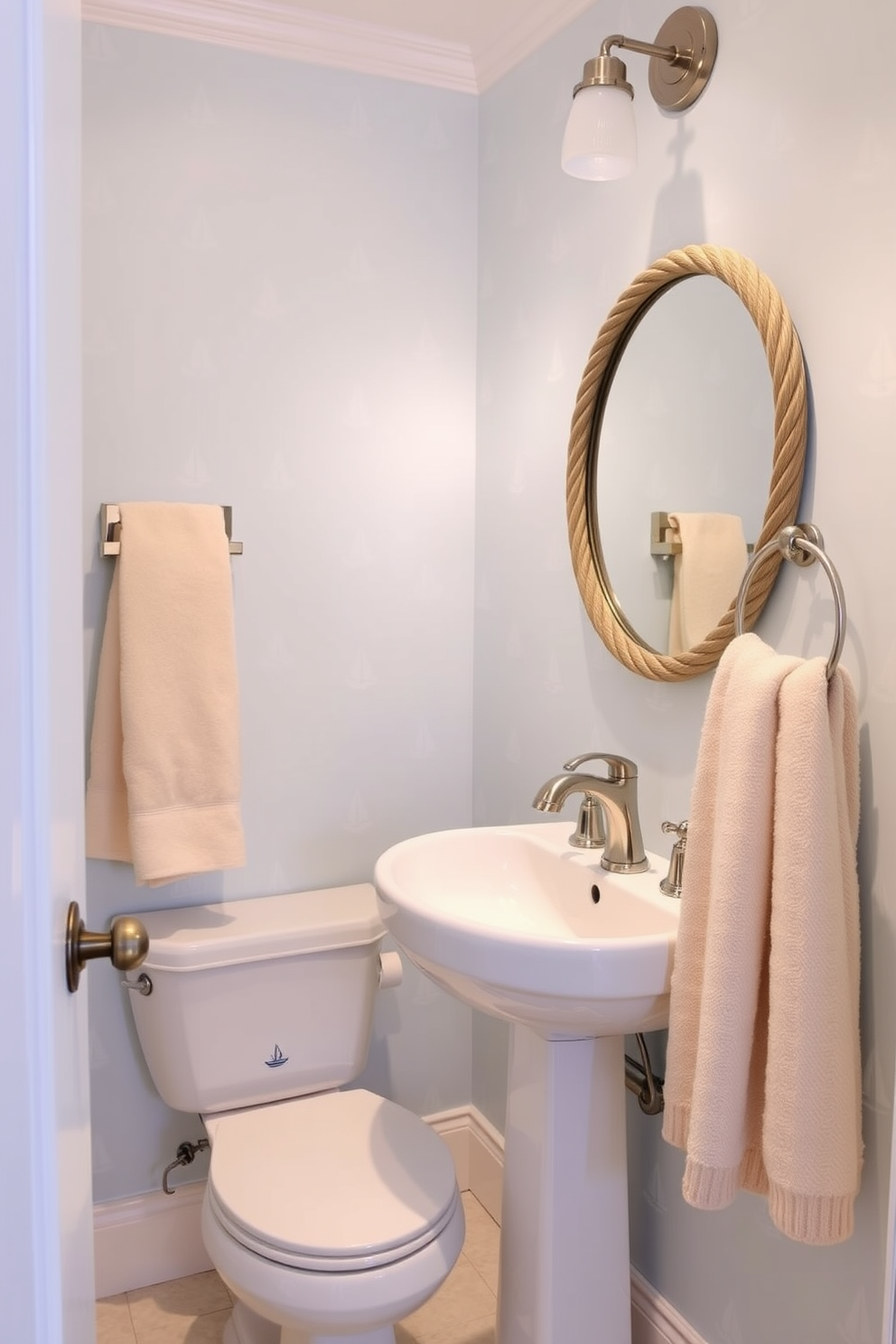 A charming powder room featuring nautical themes with soft colors. The walls are adorned with light blue wallpaper decorated with subtle white sailboat patterns. A sleek white pedestal sink sits against the wall, complemented by a round mirror with a rope-like frame. Soft beige towels hang neatly from a brushed nickel towel rack, adding a touch of warmth to the coastal-inspired space.