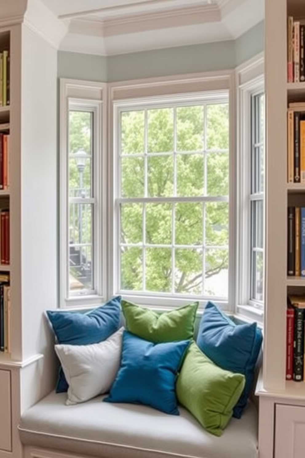 A bright window seat is adorned with plush cushions in various shades of blue and green, creating a cozy nook for relaxation and reading. Surrounding the window are built-in bookshelves filled with an eclectic mix of books and decorative items, enhancing the inviting atmosphere of the room.